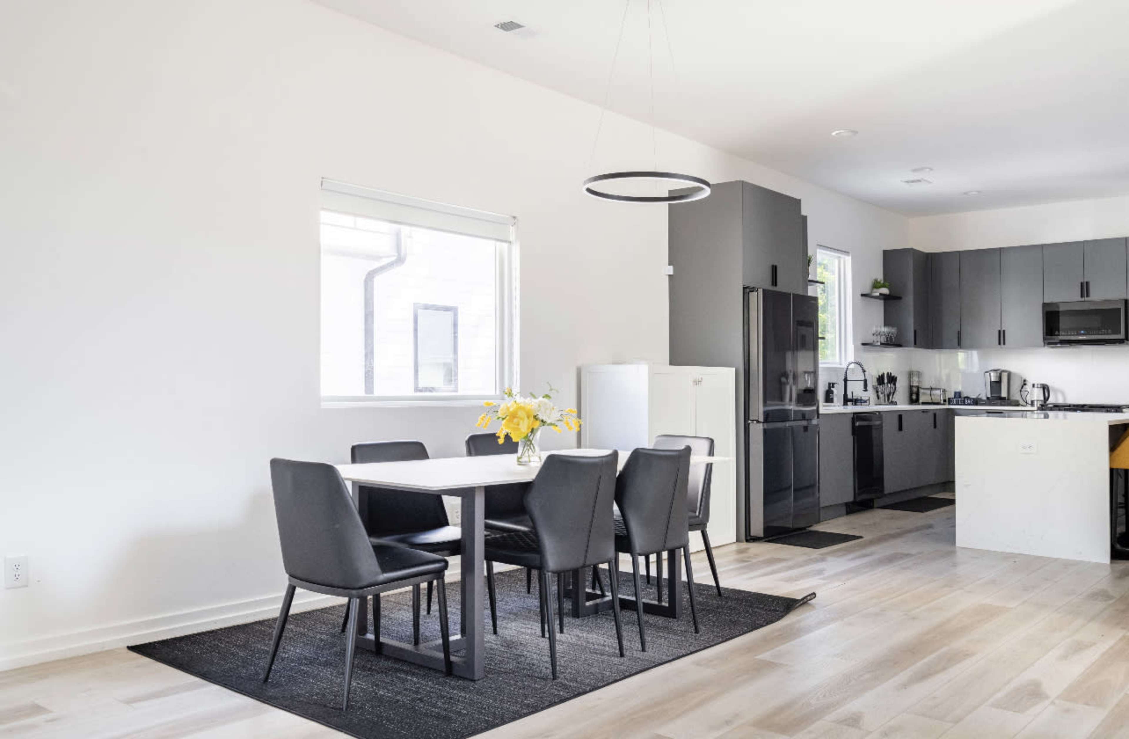 A modern kitchen and dining area features a table with six chairs, a refrigerator, and dark cabinetry.
