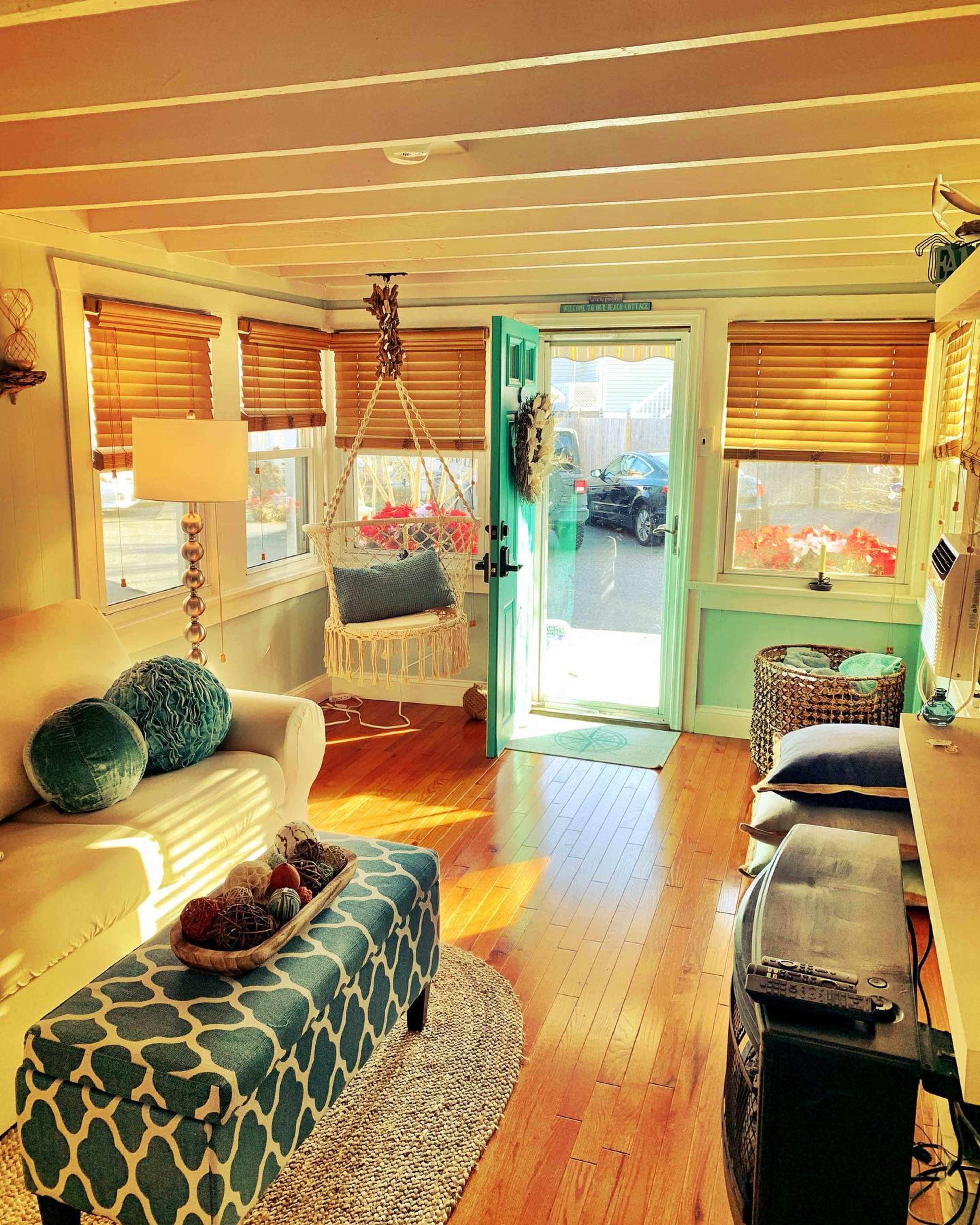 A cozy living room featuring a hanging chair, a turquoise door, and large windows with wooden blinds.