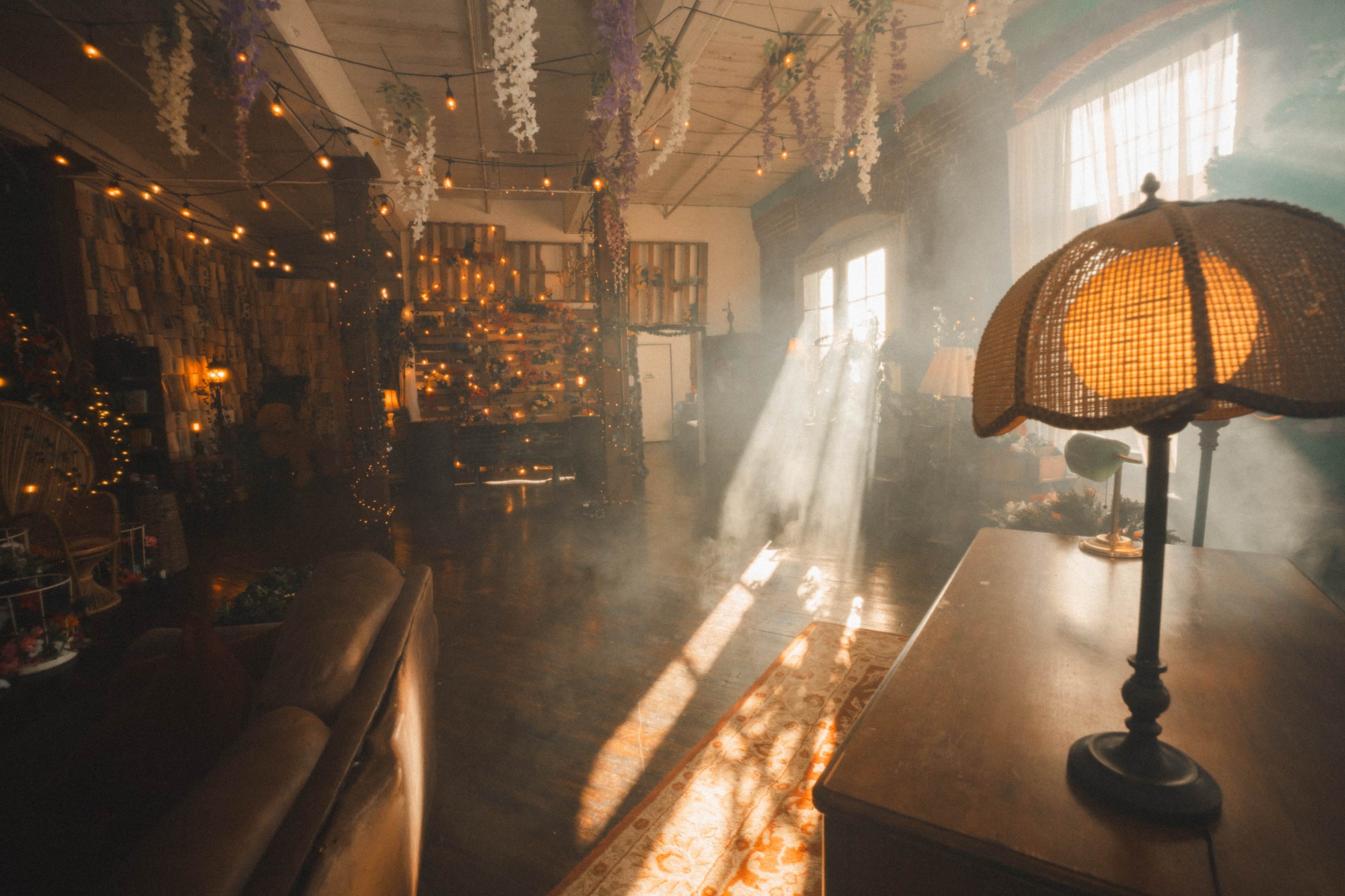 A cozy room filled with soft lighting, featuring a vintage lamp and illuminated wooden surfaces, surrounded by decorative elements and a smoky atmosphere.