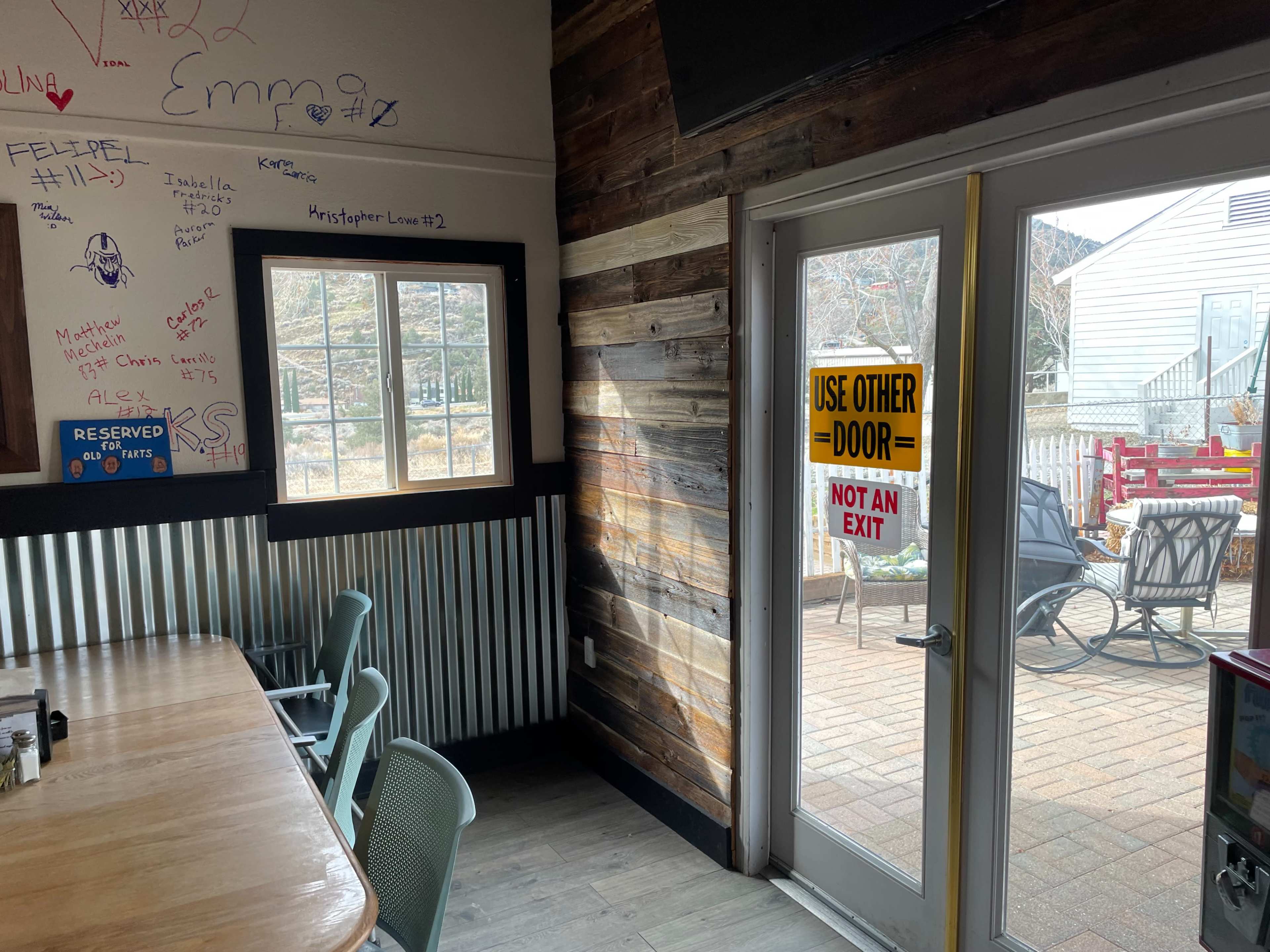 The interior corner of a rustic restaurant with wooden walls, a table, and a door marked "USE OTHER DOOR - NOT AN EXIT."