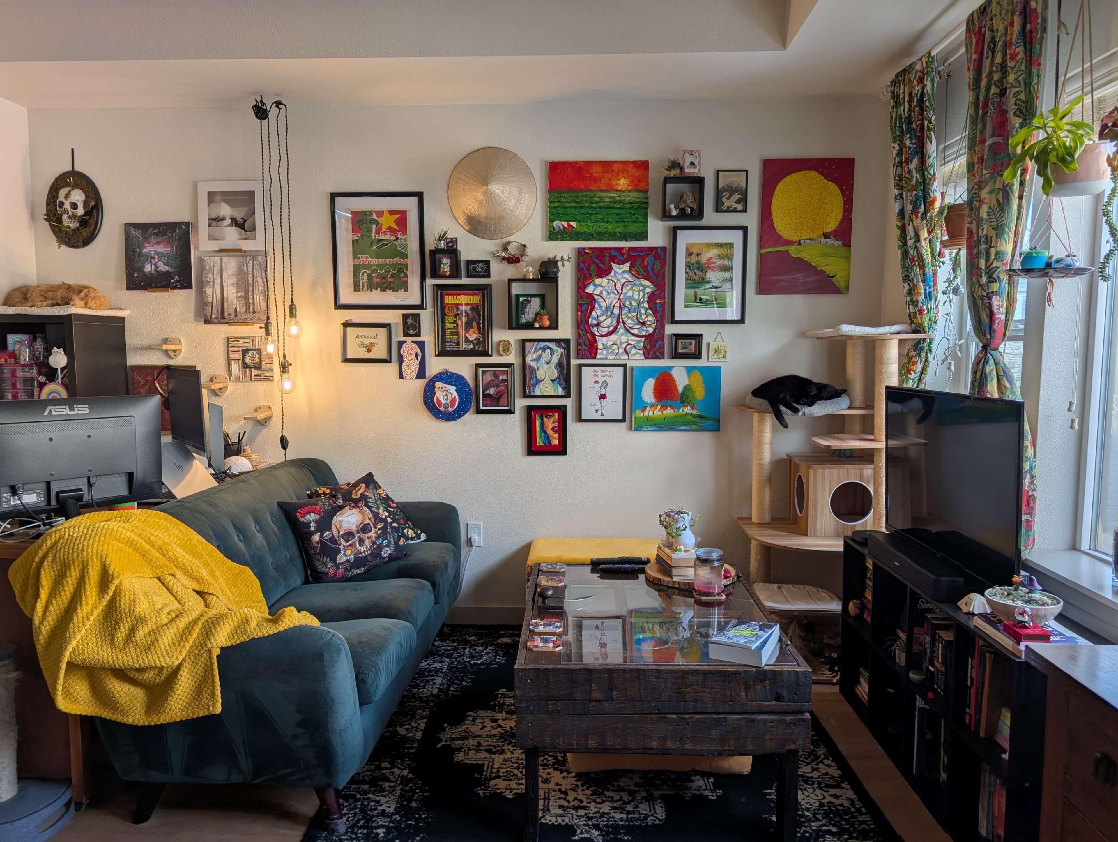 The scene depicts a cozy living room with a green couch, a variety of framed artworks on the walls, and a wooden coffee table at the center, surrounded by decorative items and a tall cat tree.