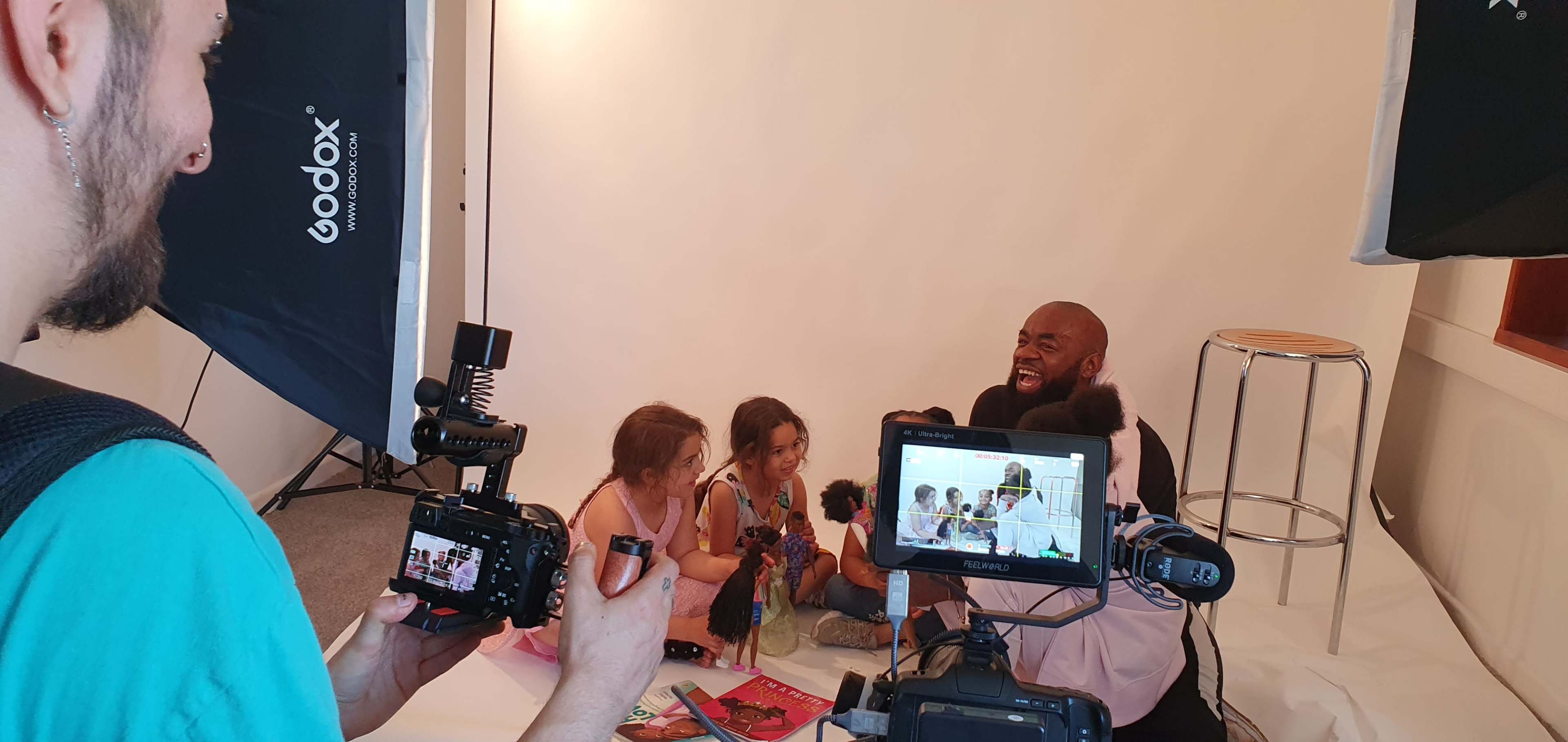 A man and three young girls are sitting on the floor in a photography studio, surrounded by cameras and lighting equipment.