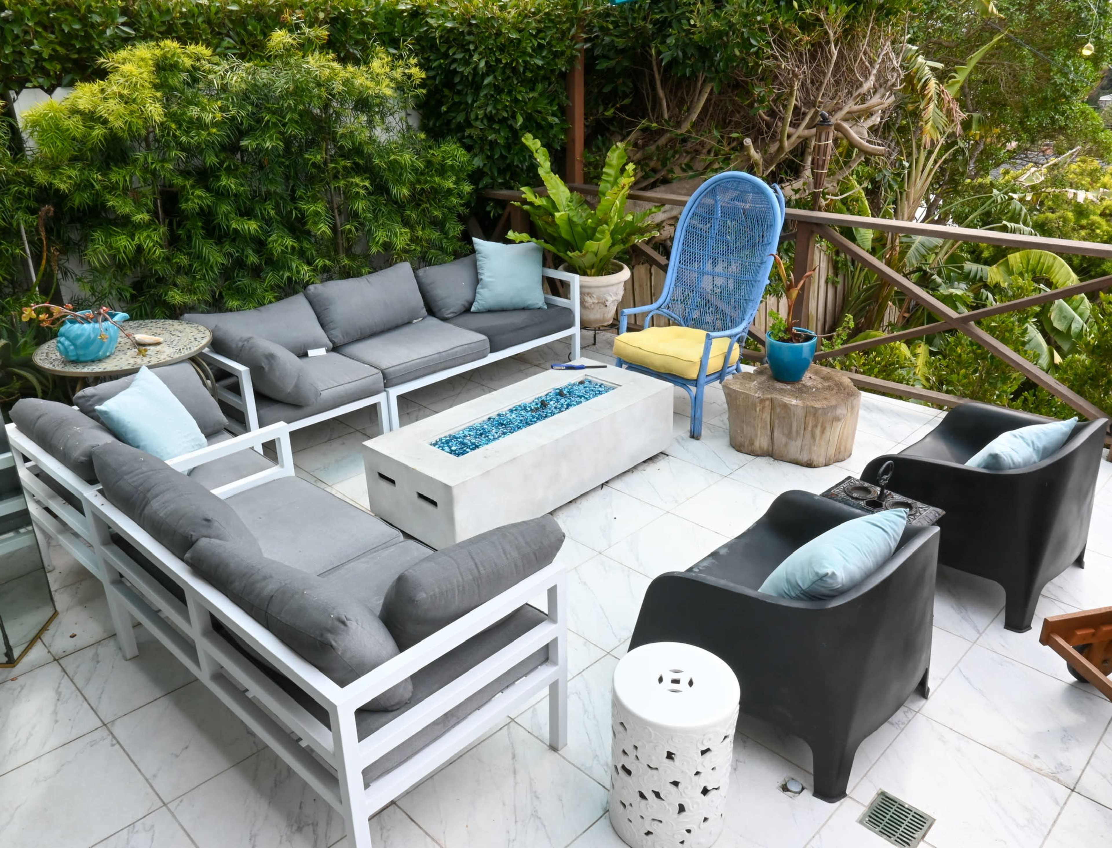 A modern outdoor seating area features a concrete fire pit surrounded by gray cushioned sofas and chairs with colorful accents.