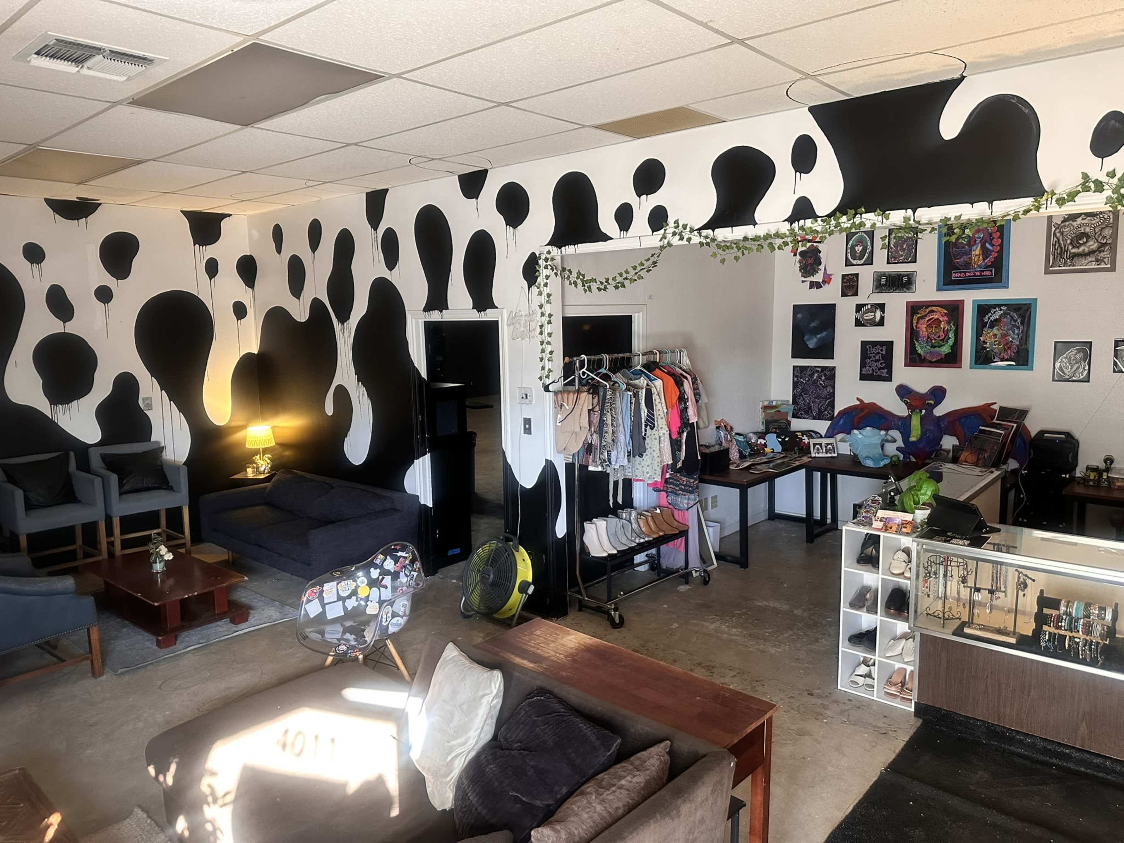 The interior of a boutique features a black and white patterned wall, a mix of seating areas, clothing racks, and various decorations on display.