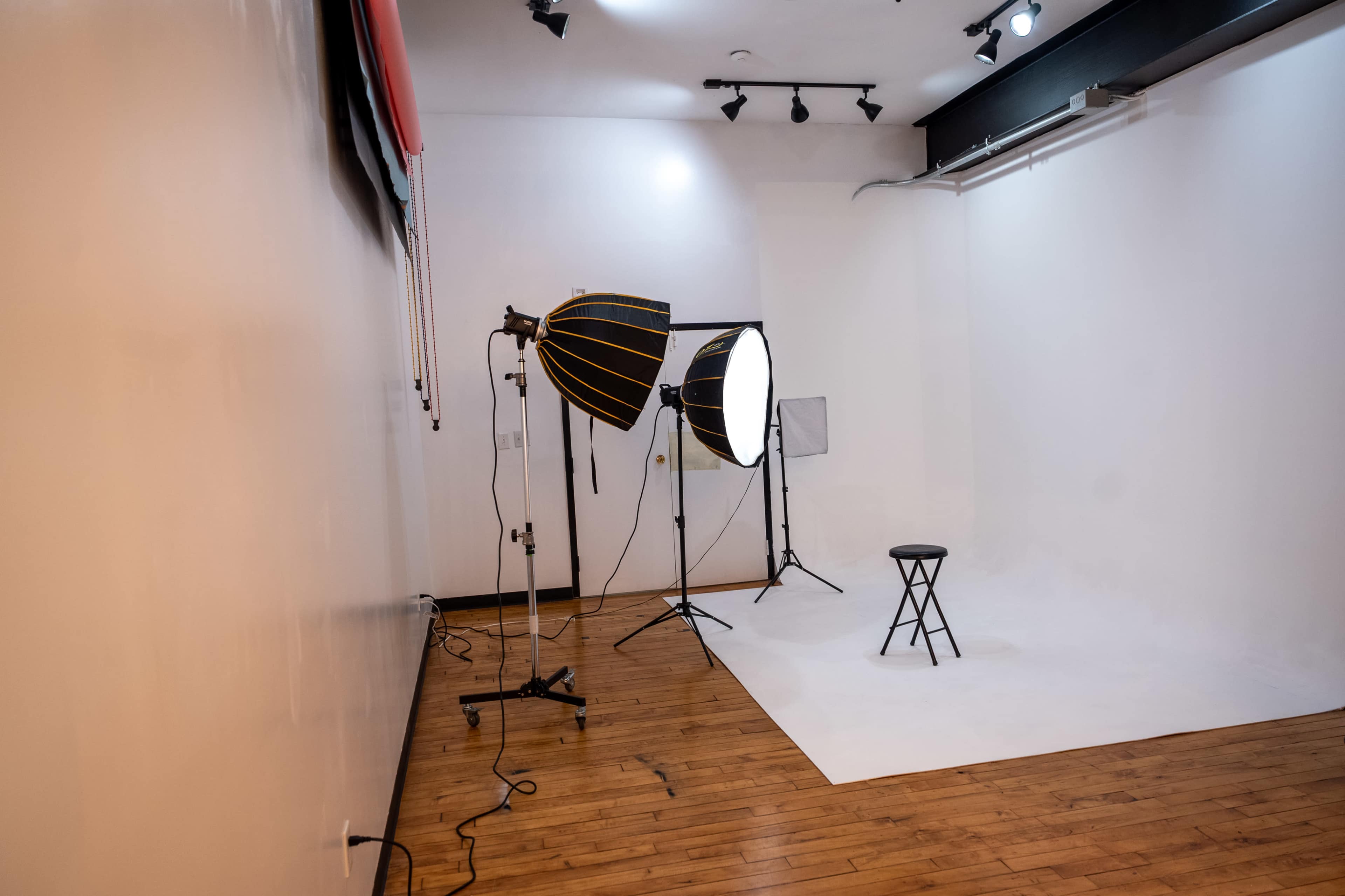 The image shows a photography studio setup featuring two large softbox lights pointed at a small black stool placed on a white backdrop.