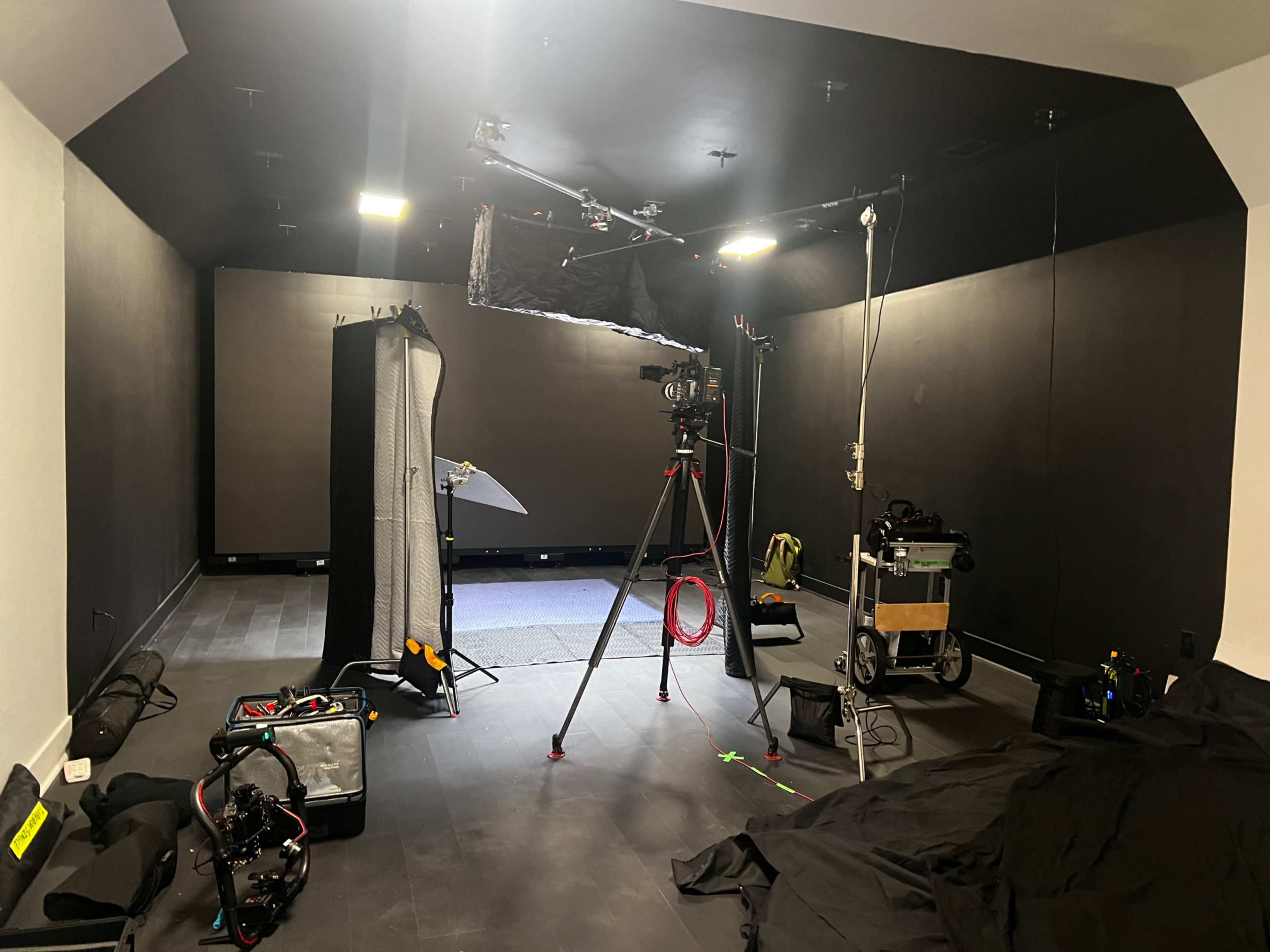 A photography or film studio equipped with a camera on a tripod, lighting equipment, and various accessories arranged on the floor.