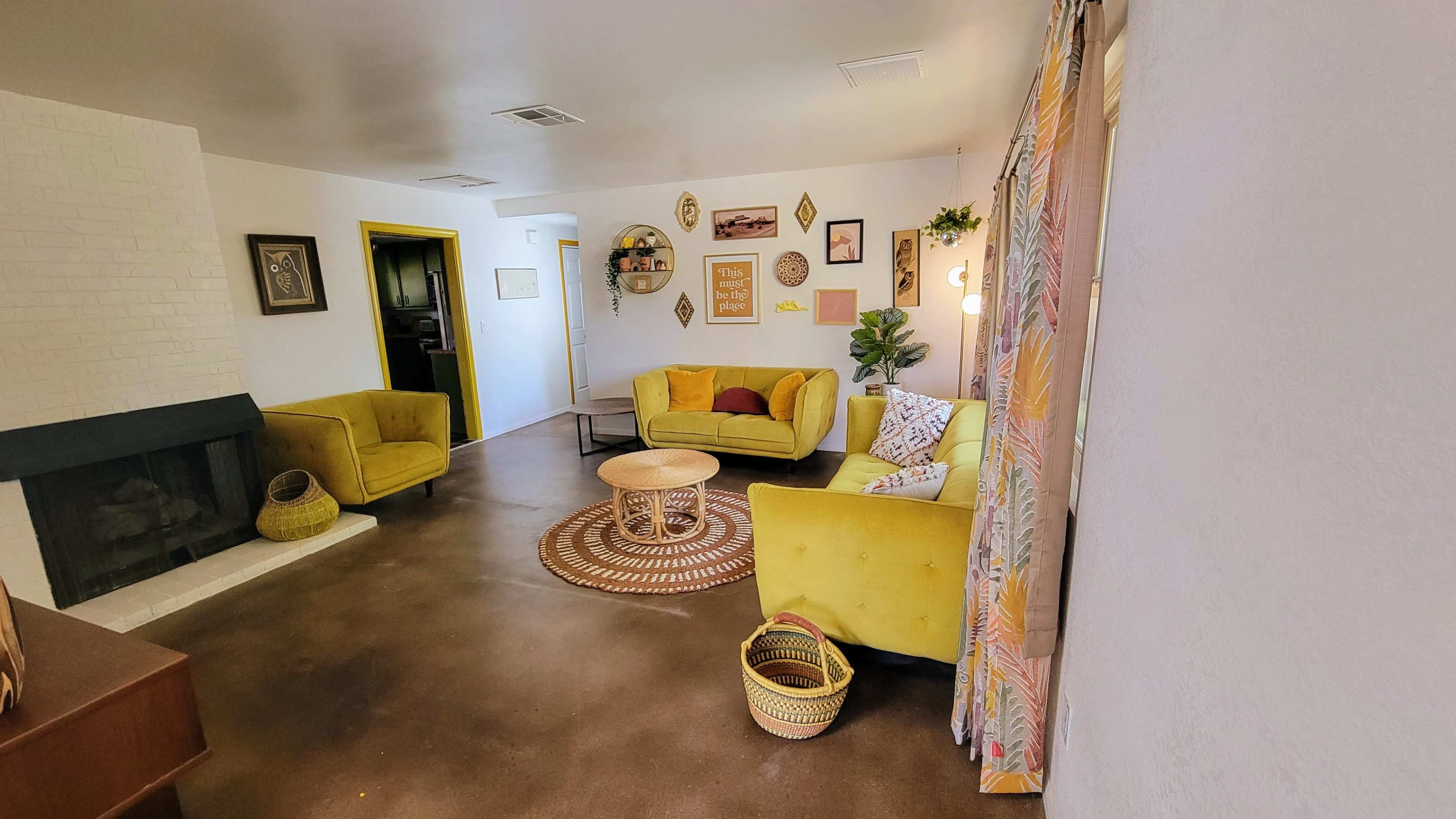 A living room features yellow chairs, a round coffee table, and various wall decorations, with a fireplace in the corner.
