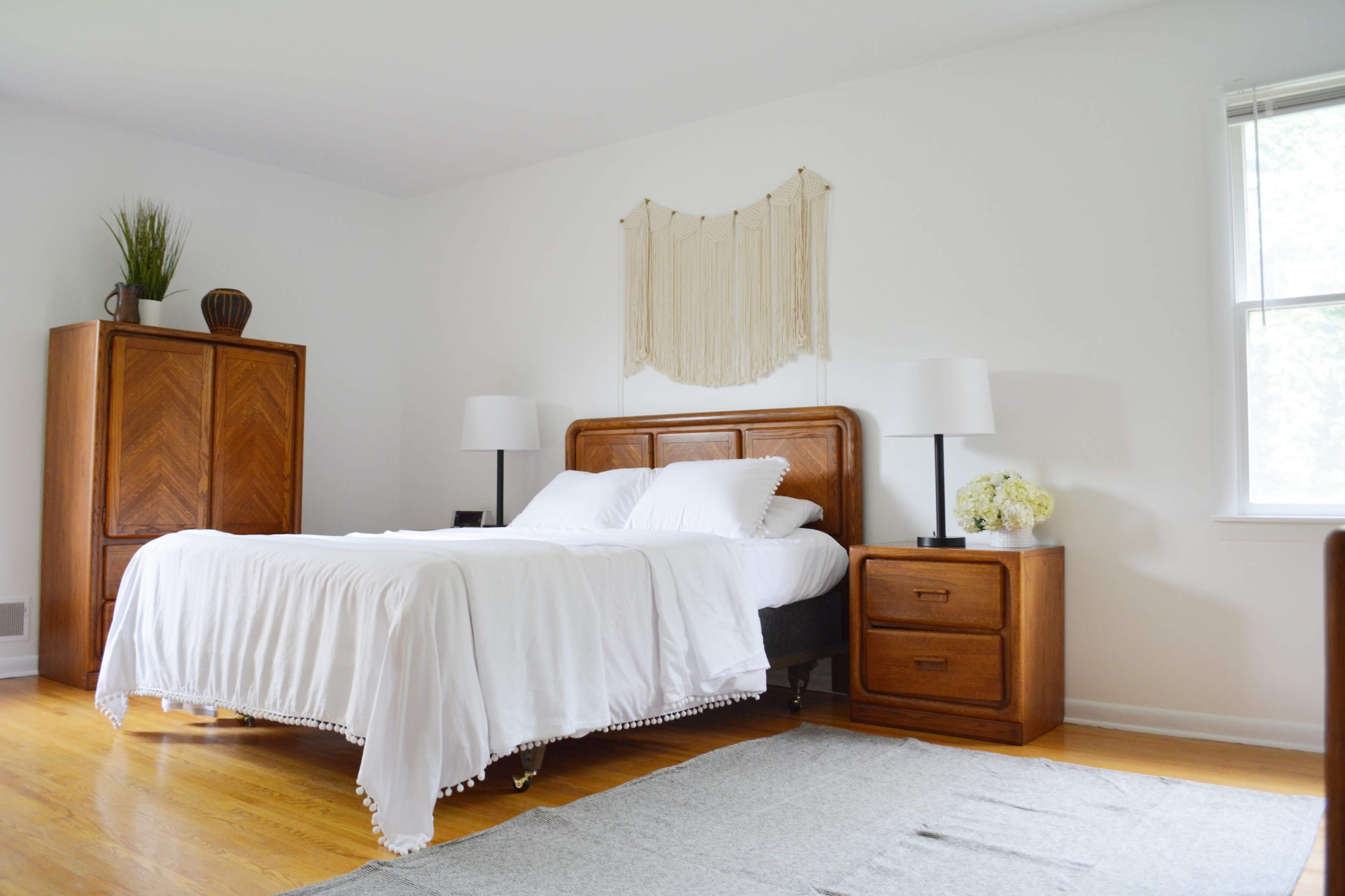 A simple bedroom with a wooden bed, nightstands, and a wardrobe, all set against white walls and a wooden floor.