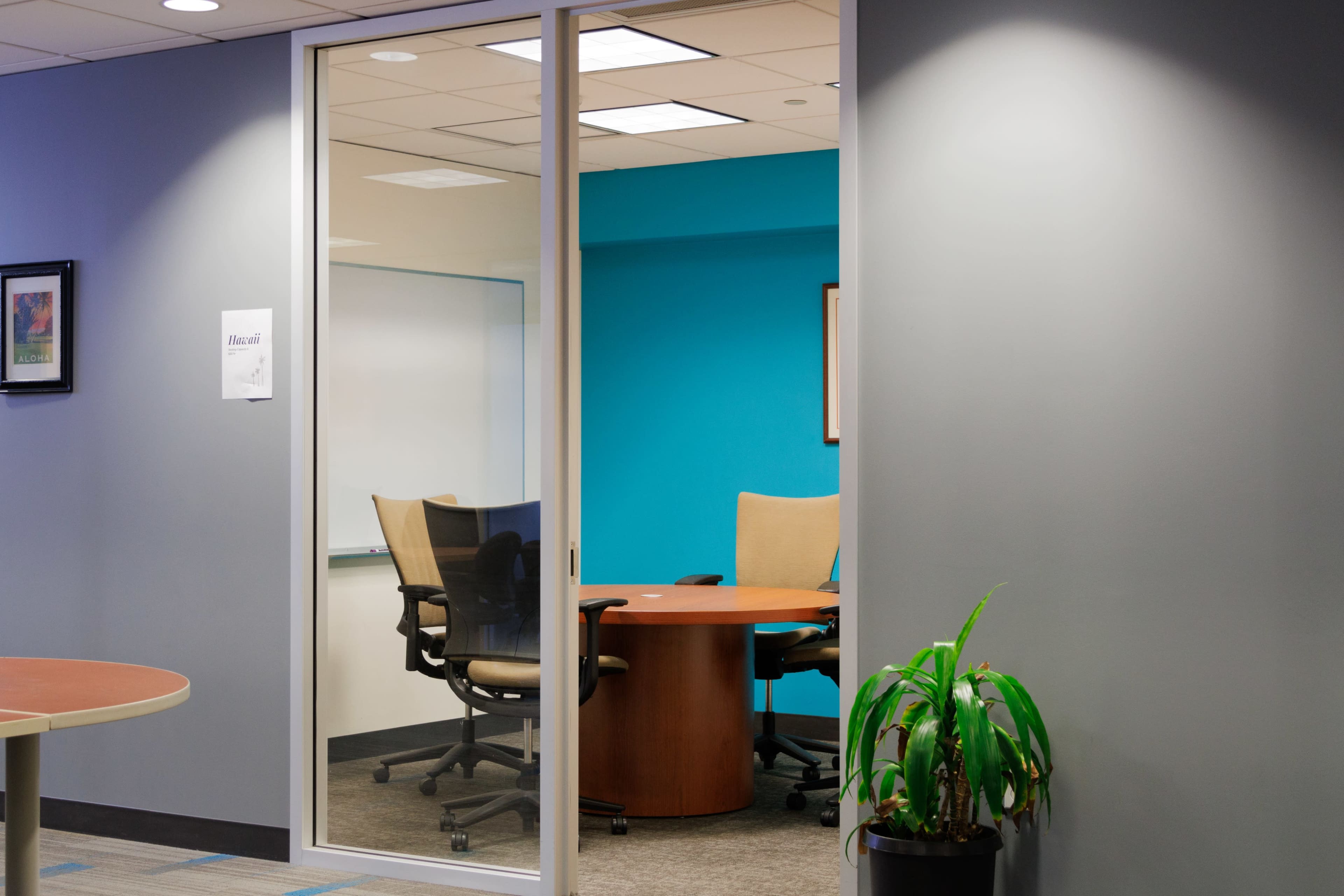 A glass-walled conference room features a round table and several chairs, with a blue wall in the background.