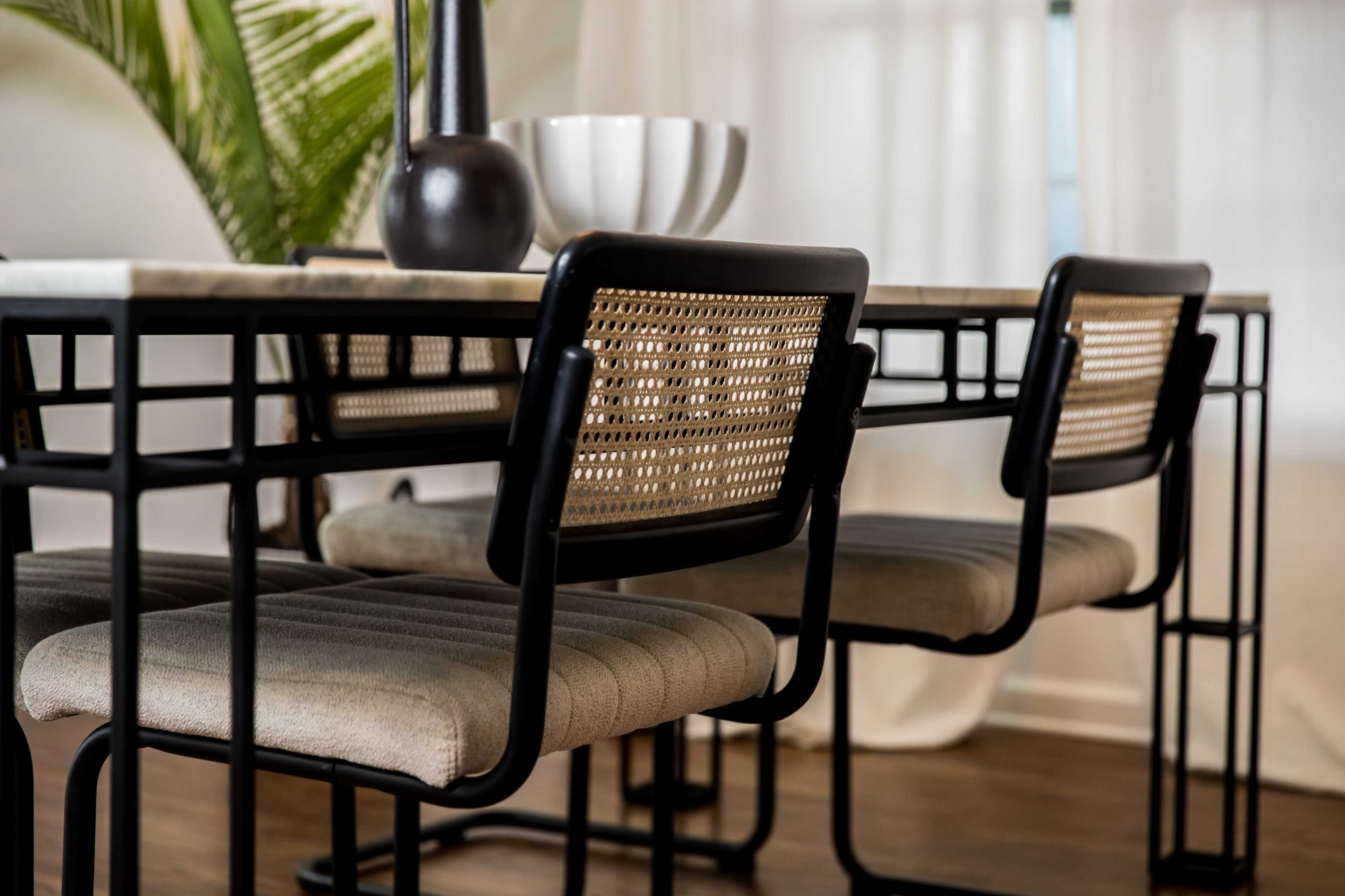A dining table with a marble top is surrounded by metal-framed chairs featuring woven cane backs and upholstered seats.