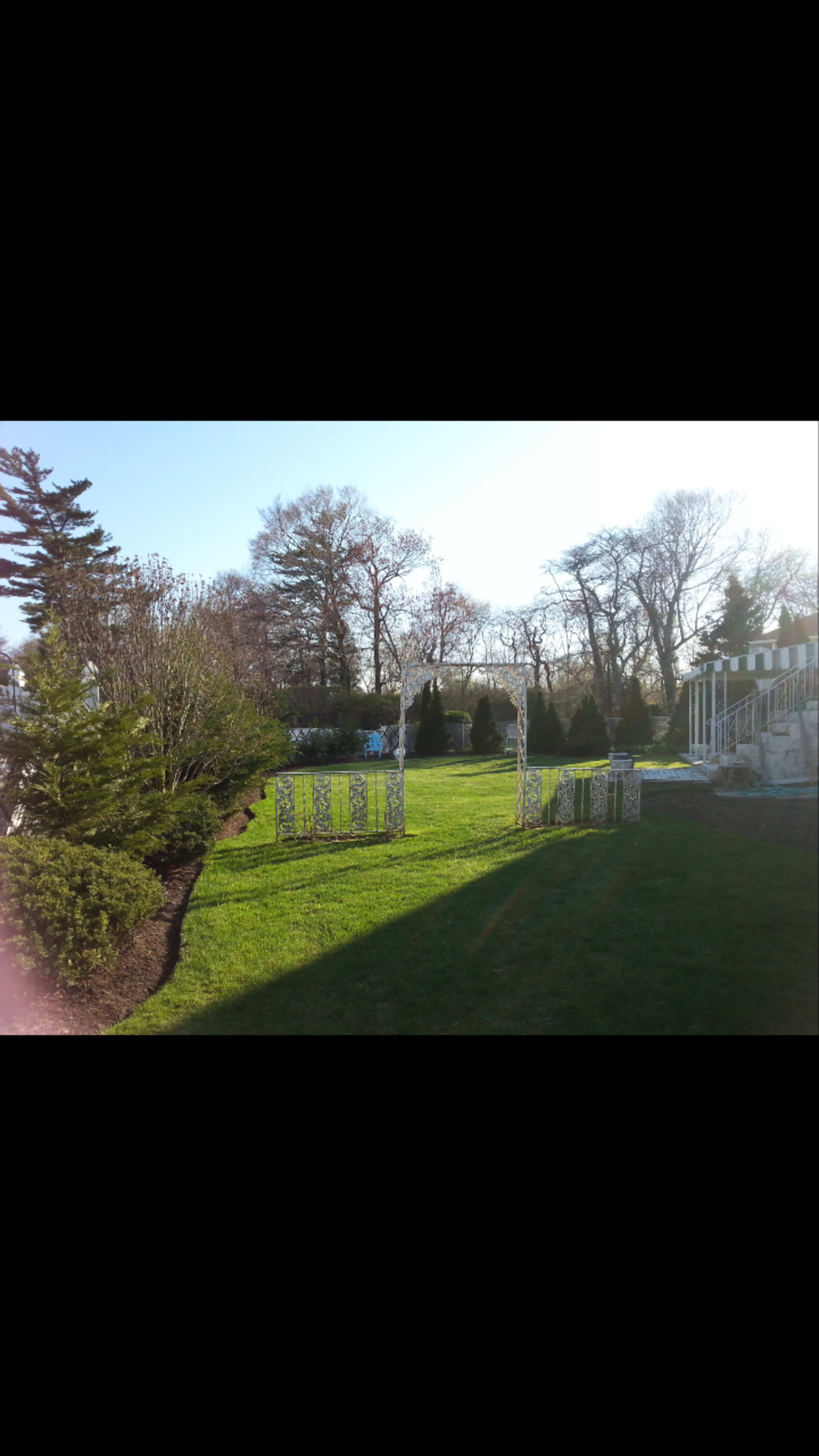 A landscaped garden with green grass, trees in the background, and a white trellis at the edge of the lawn.