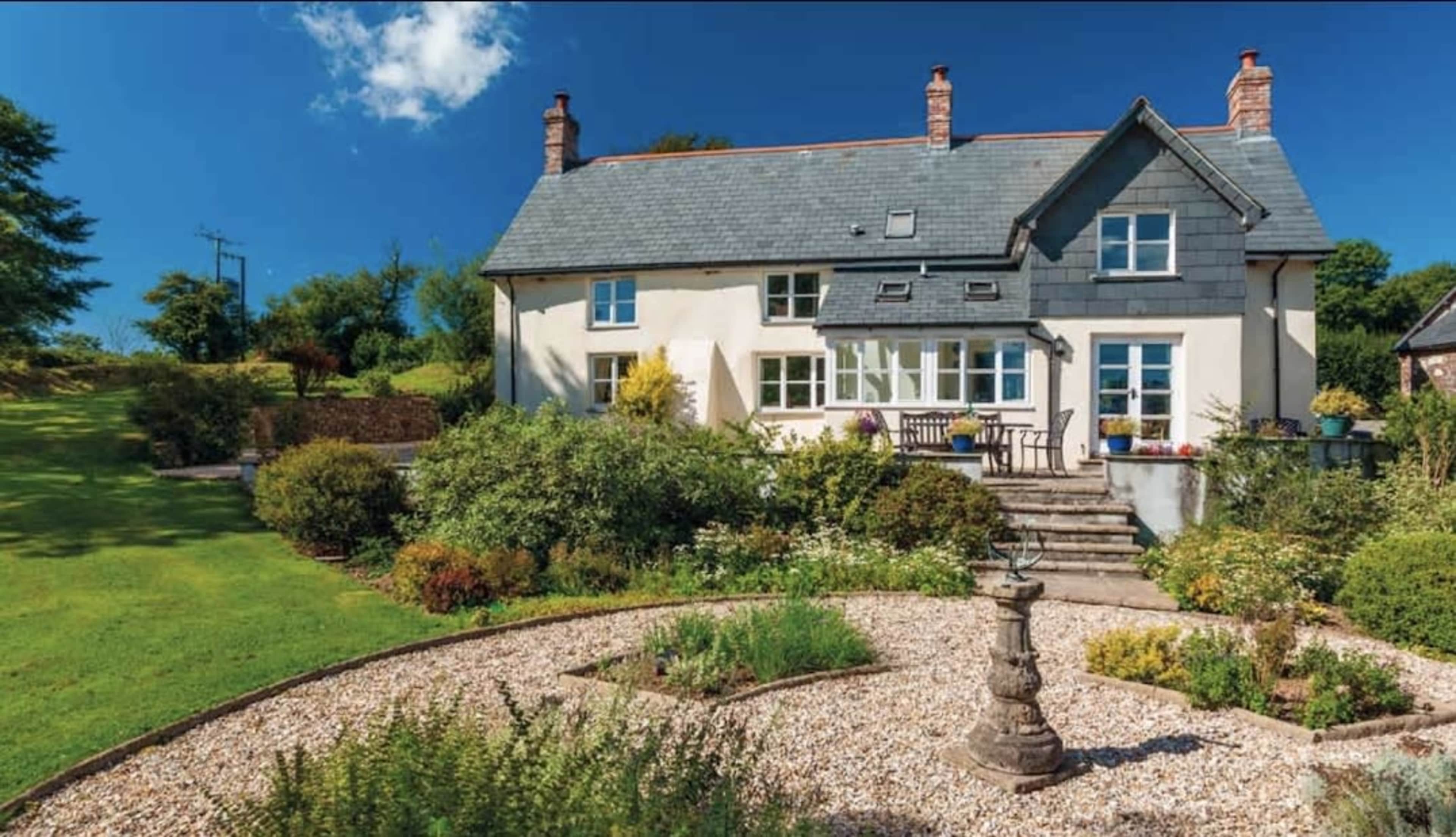 A two-story house with a gray roof is surrounded by a landscaped garden and a pathway.