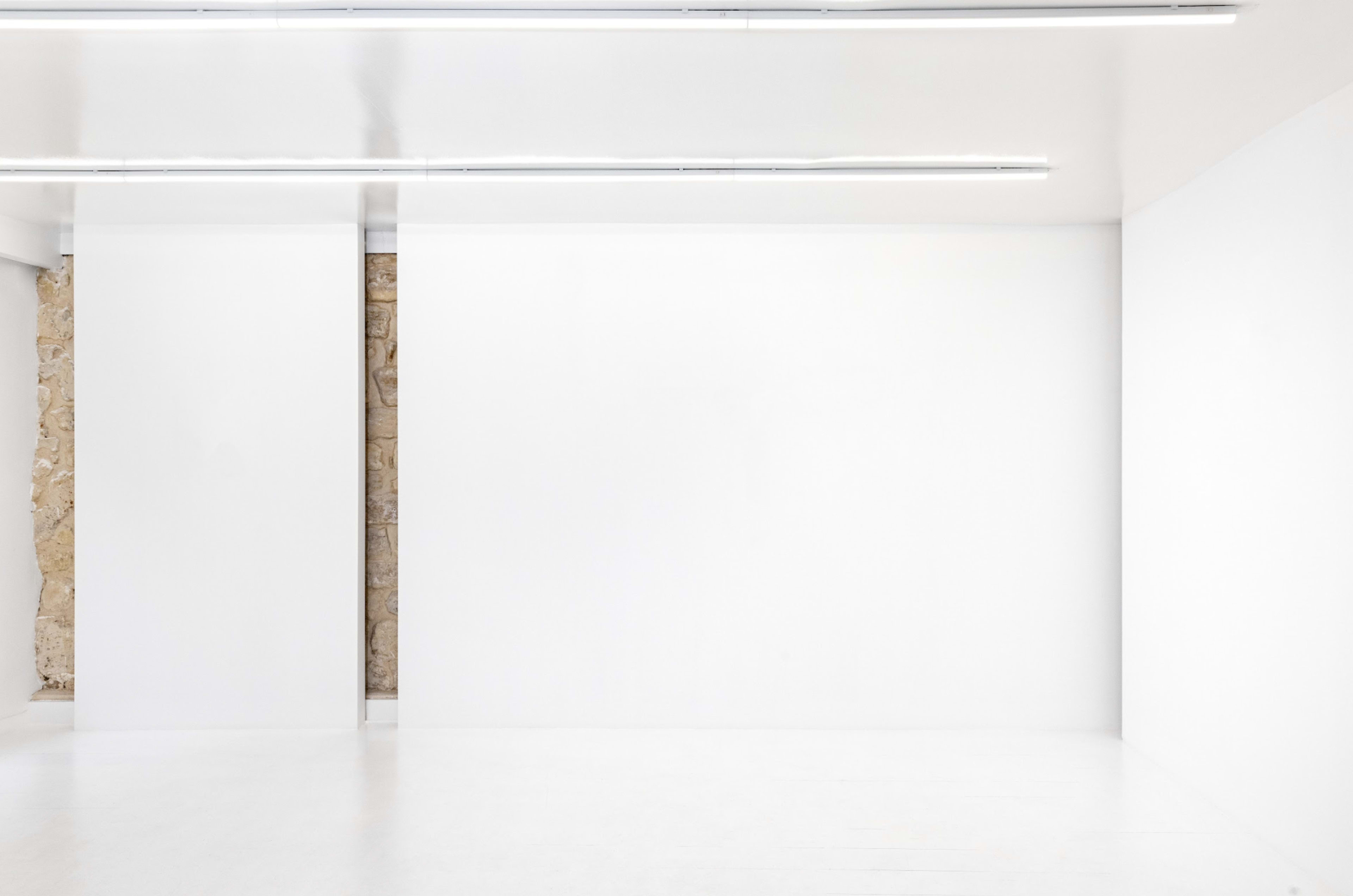 The image shows a minimalist interior space featuring white walls and fluorescent lighting.