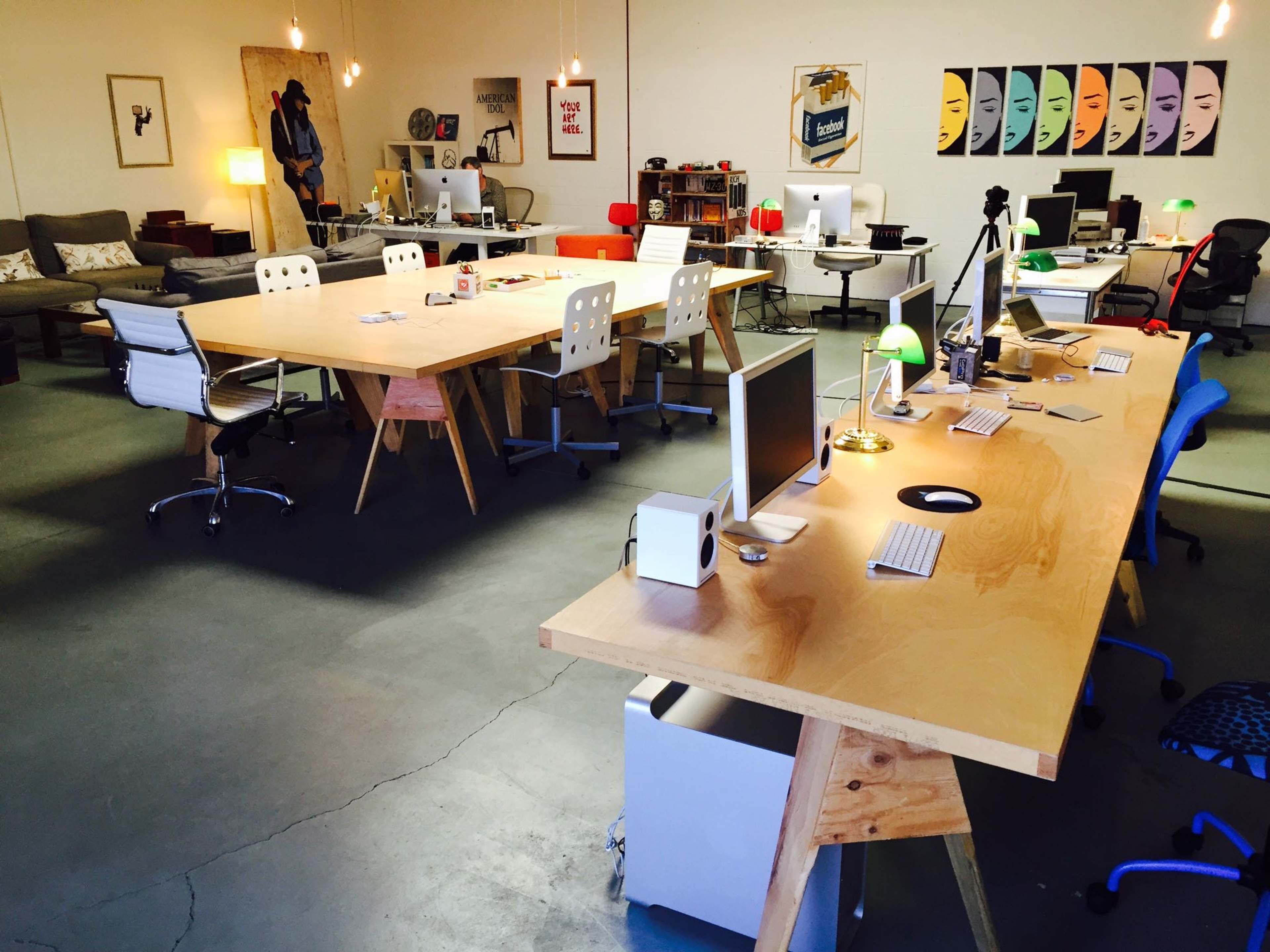 The image shows a modern office space with multiple desks, computers, and a lounge area that features comfortable seating.