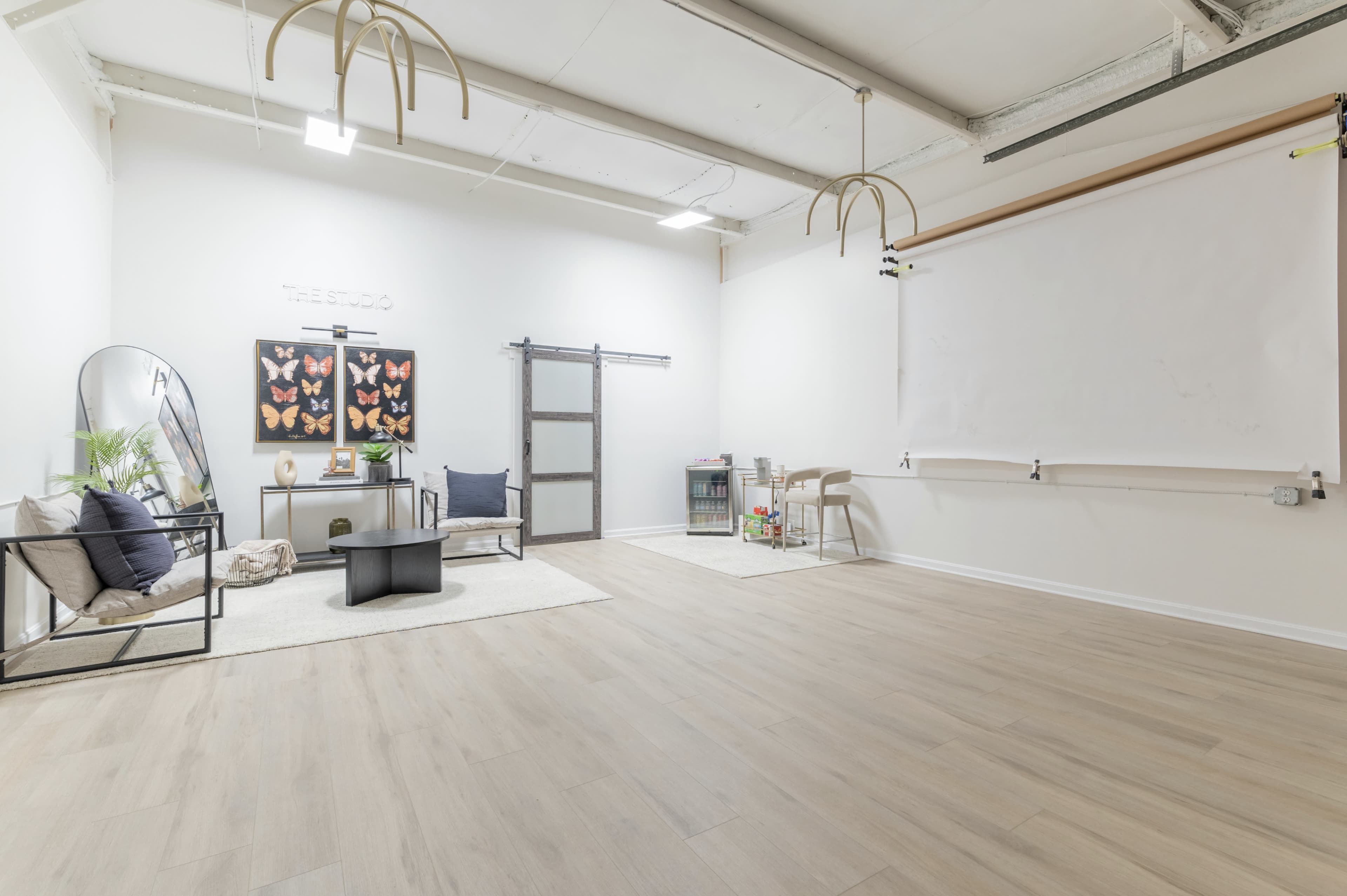 A modern, minimalist studio space with wooden flooring, a seating area, and large decorative wall art featuring butterflies.