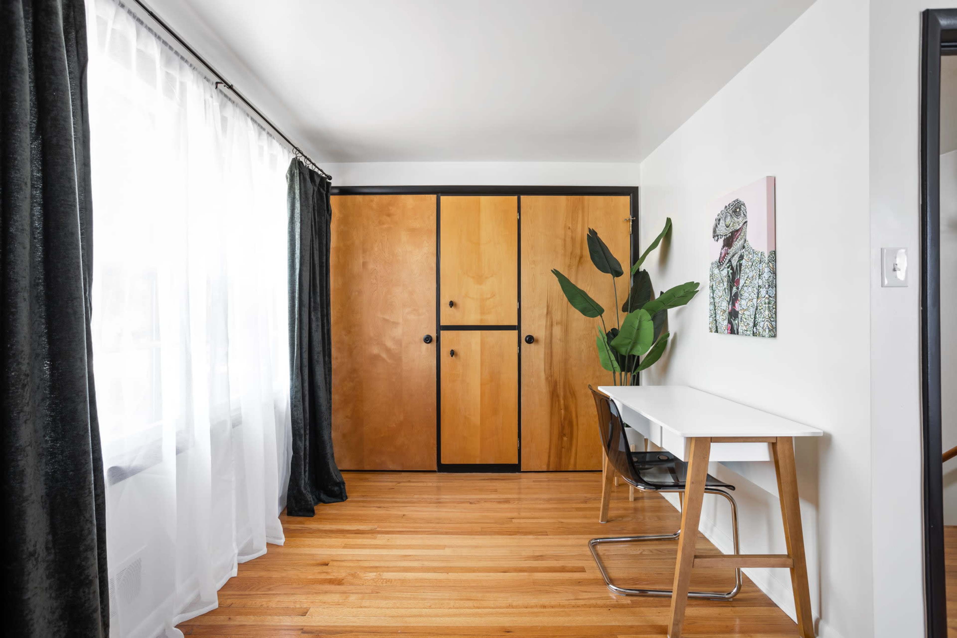 A bright room with hardwood floors, featuring a desk, a potted plant, and wooden sliding closet doors.