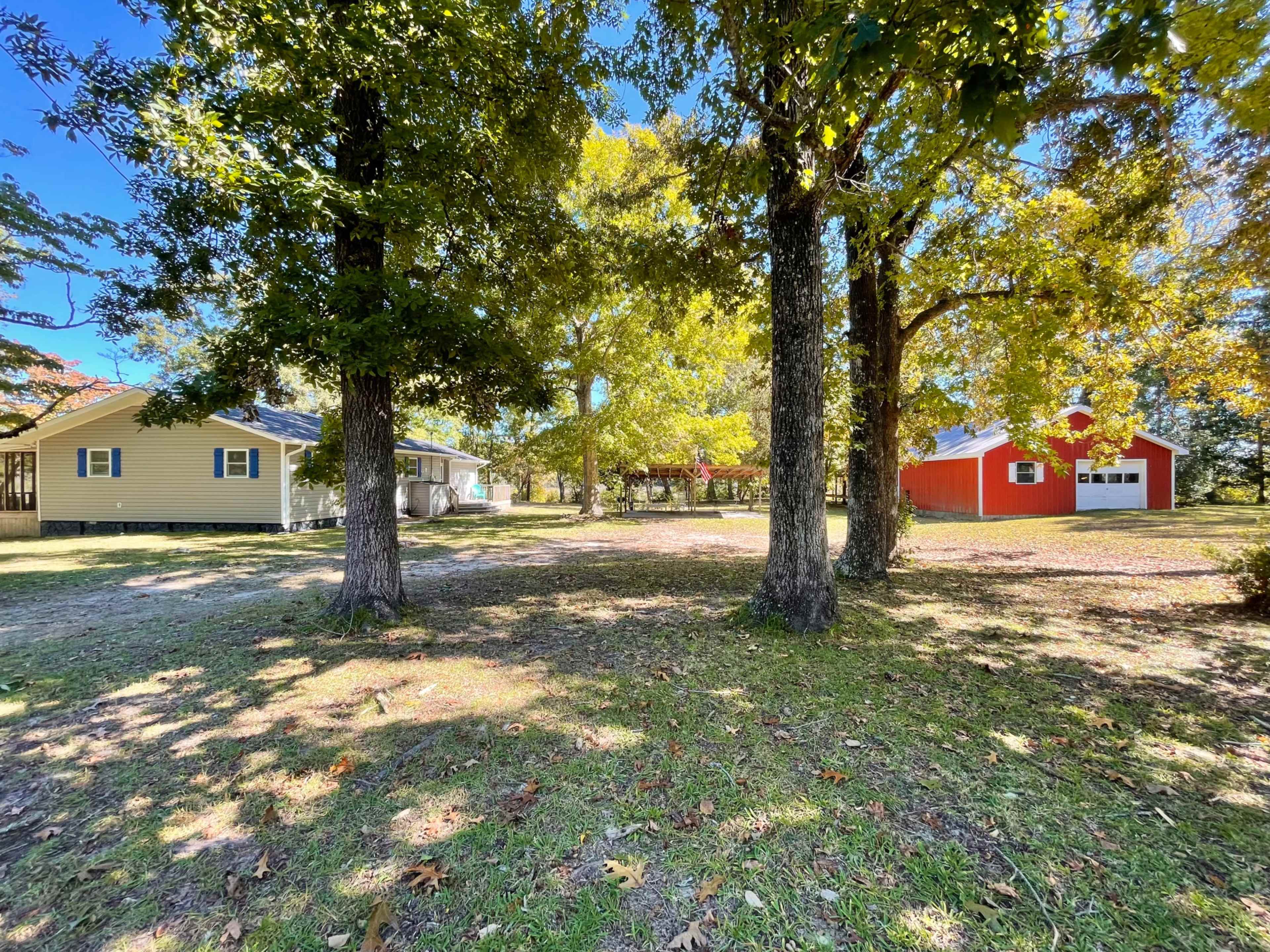 A grassy area bordered by trees, with a yellow house on the left and a red barn on the right.