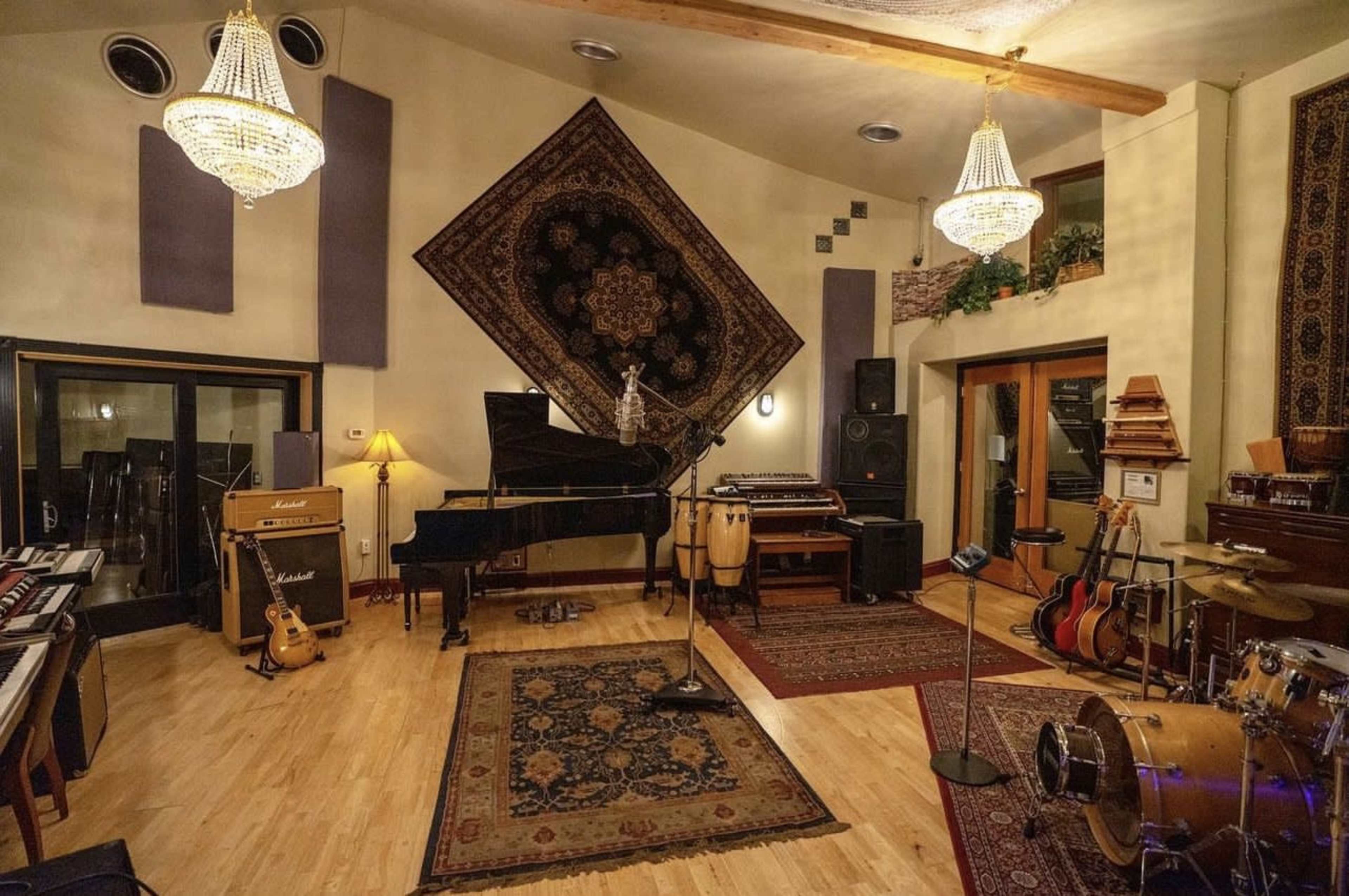 A music studio featuring a grand piano, various instruments, sound equipment, and decorative rugs under decorative lighting fixtures.