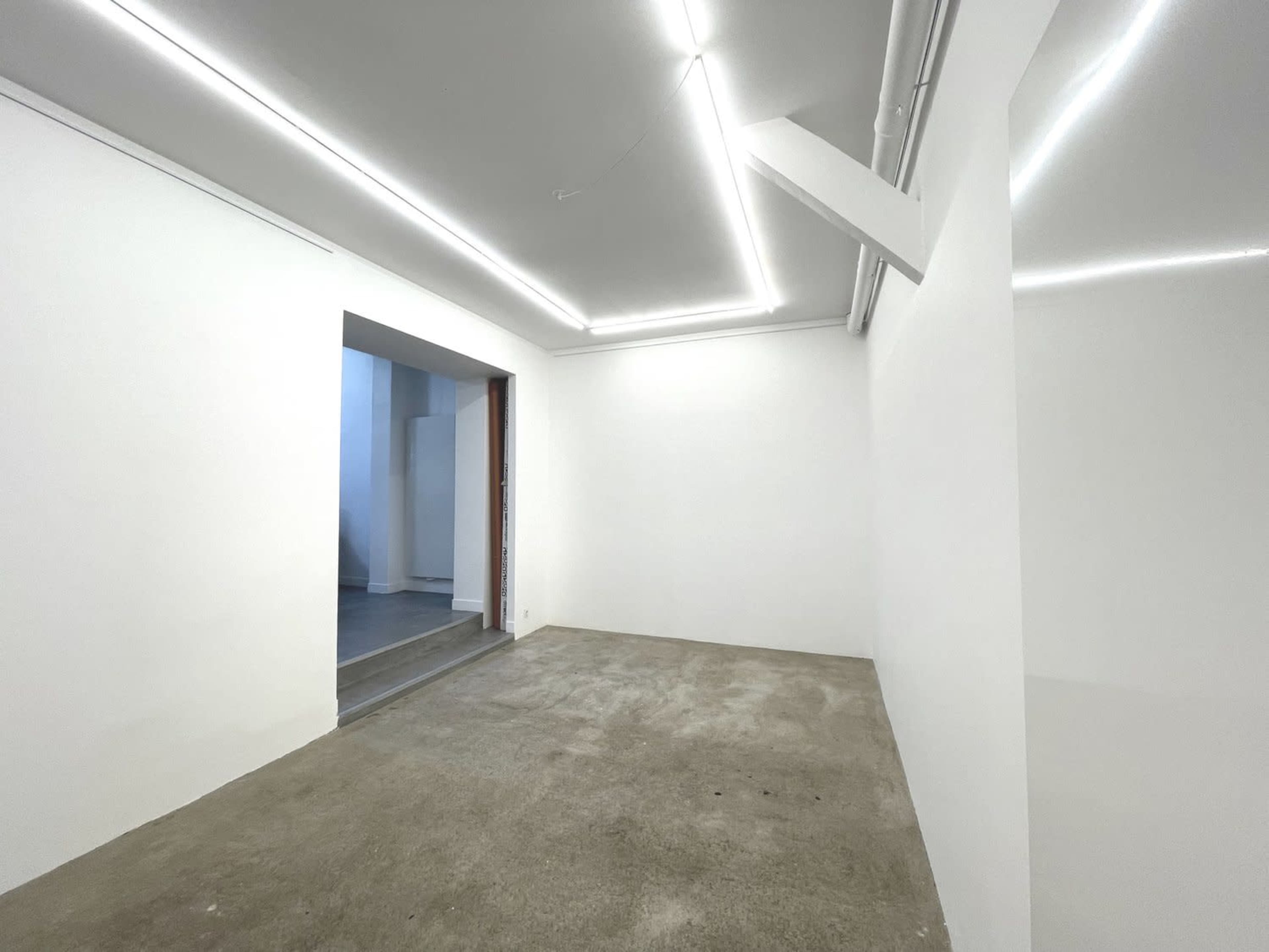 An empty room with a concrete floor and white walls features recessed lighting and an open doorway leading to a separate space.