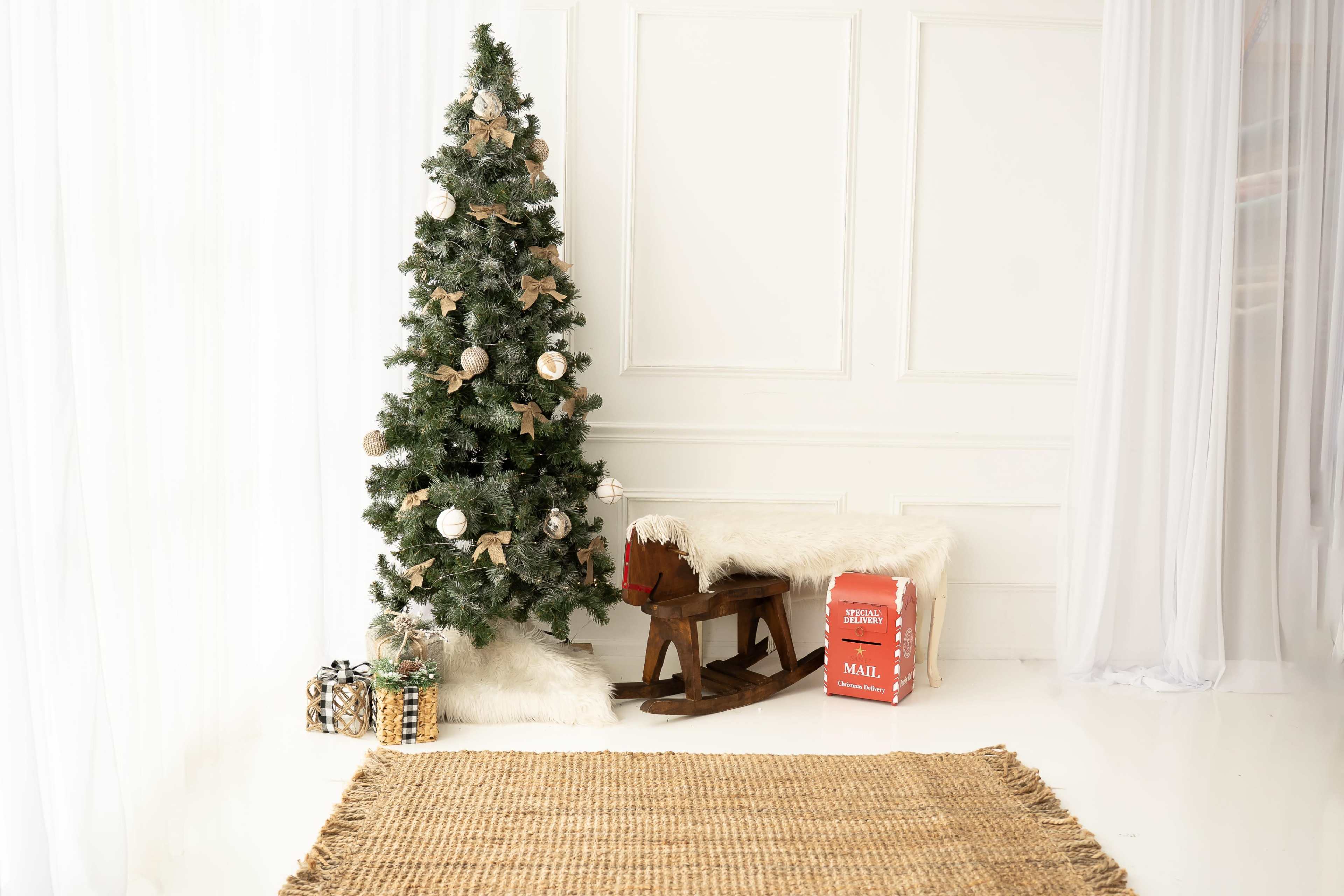 A decorated Christmas tree stands next to a rocking chair, with a gift box and a woven rug on the floor.