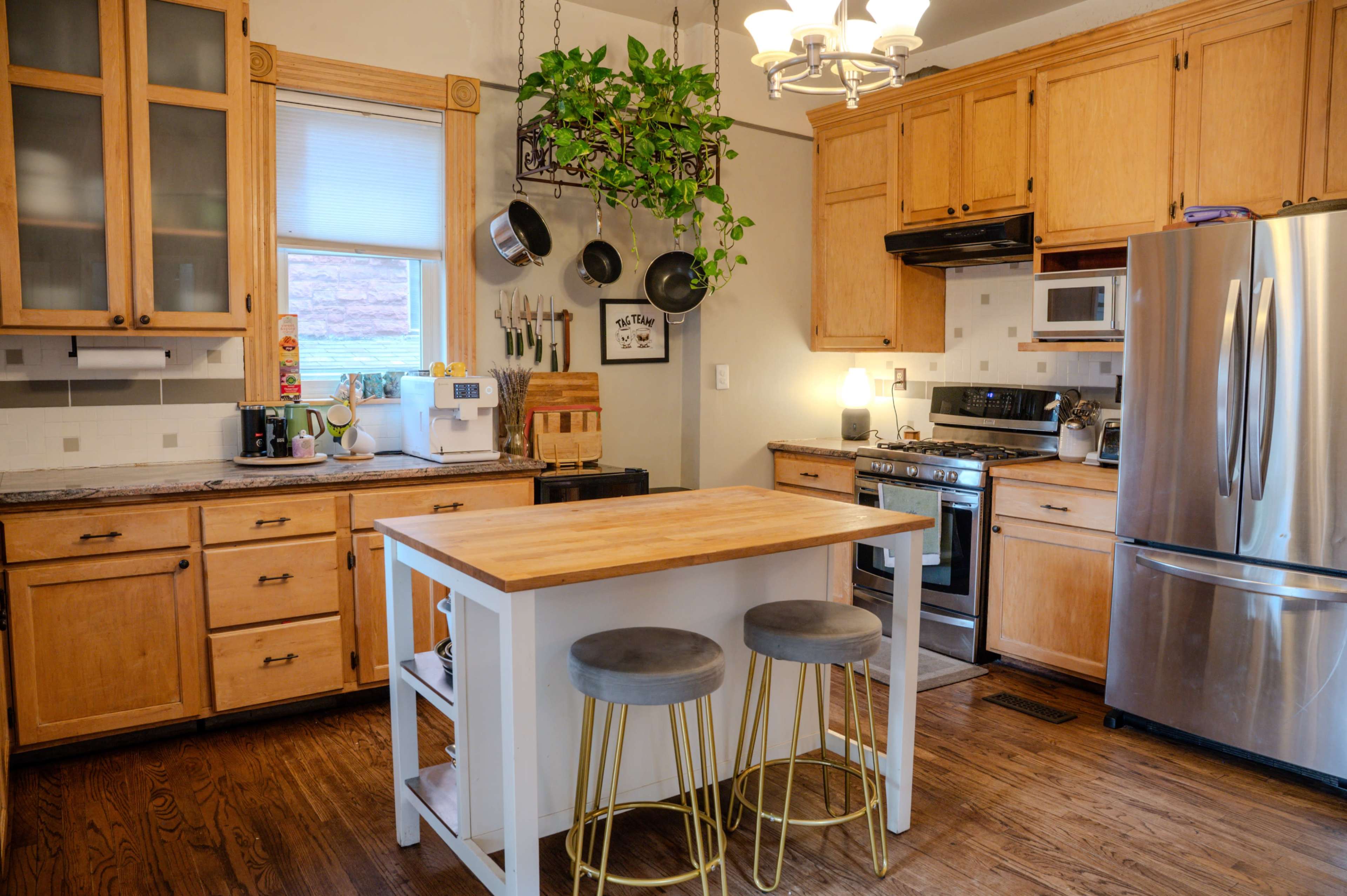 The kitchen features wooden cabinets, stainless steel appliances, a center island with seating, and hanging cookware.
