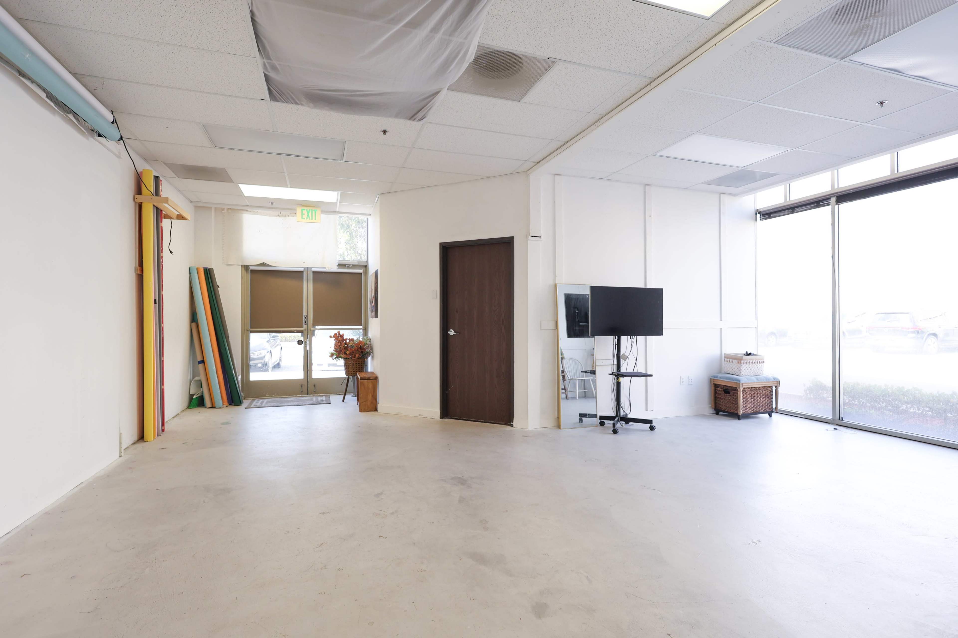 The image shows a vacant, open commercial space with a door, a television on a stand, and some decorative elements near the entrance.