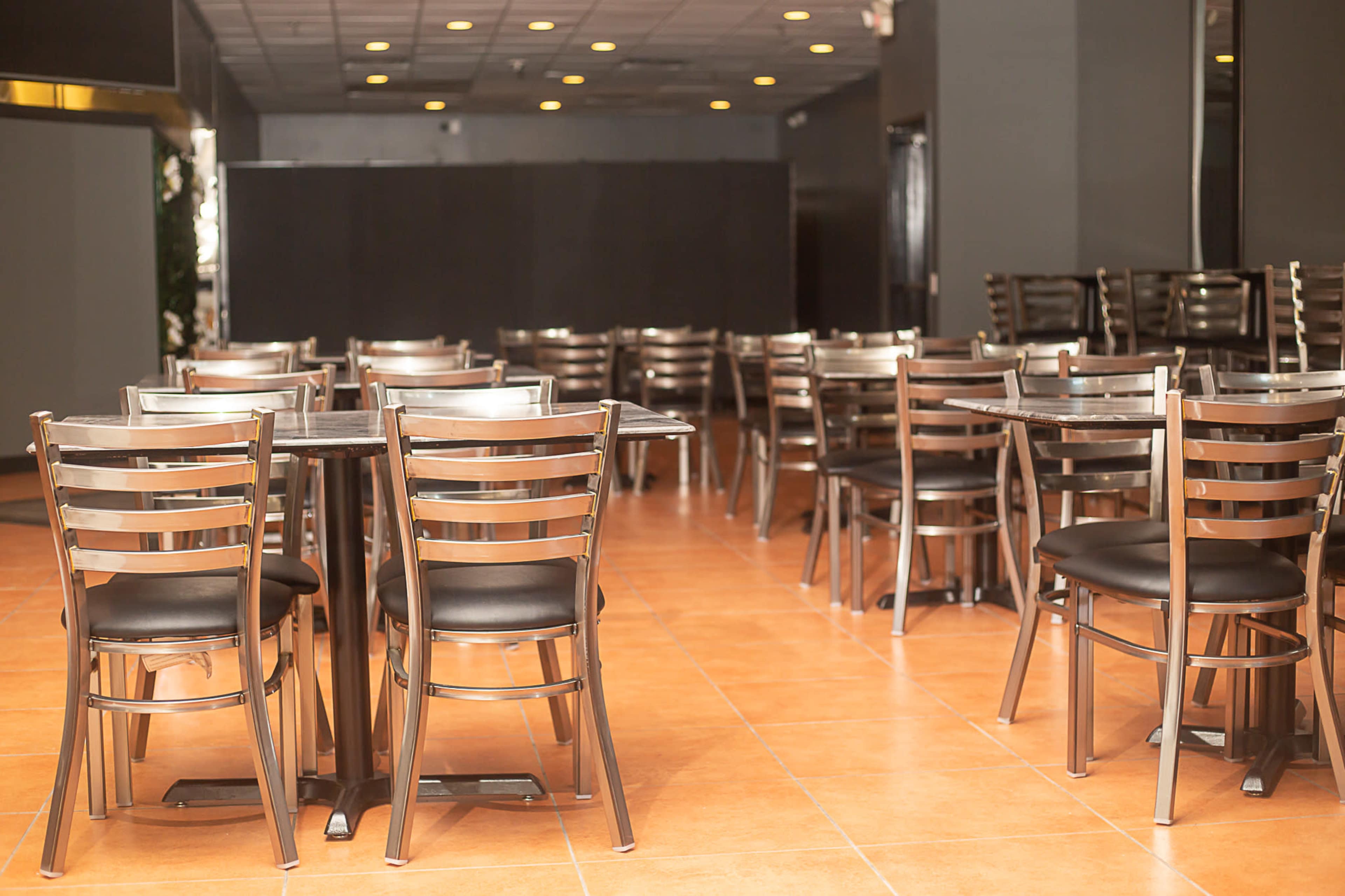 The image shows a dining area with metal-framed tables and chairs arranged neatly on a tiled floor.