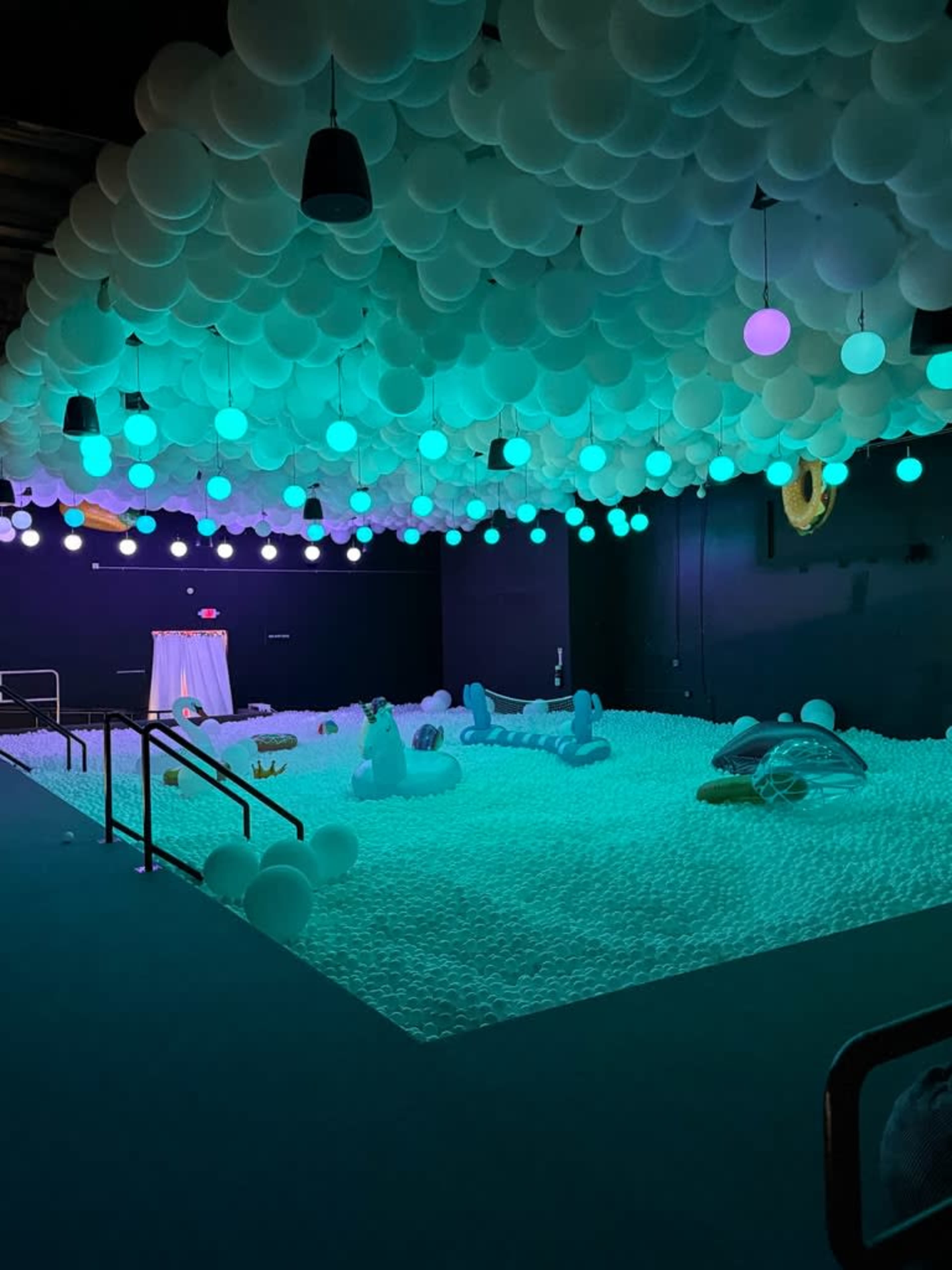 The scene features a room filled with a floor of white balls and a ceiling decorated with colorful balloons, illuminated by various glowing lights.