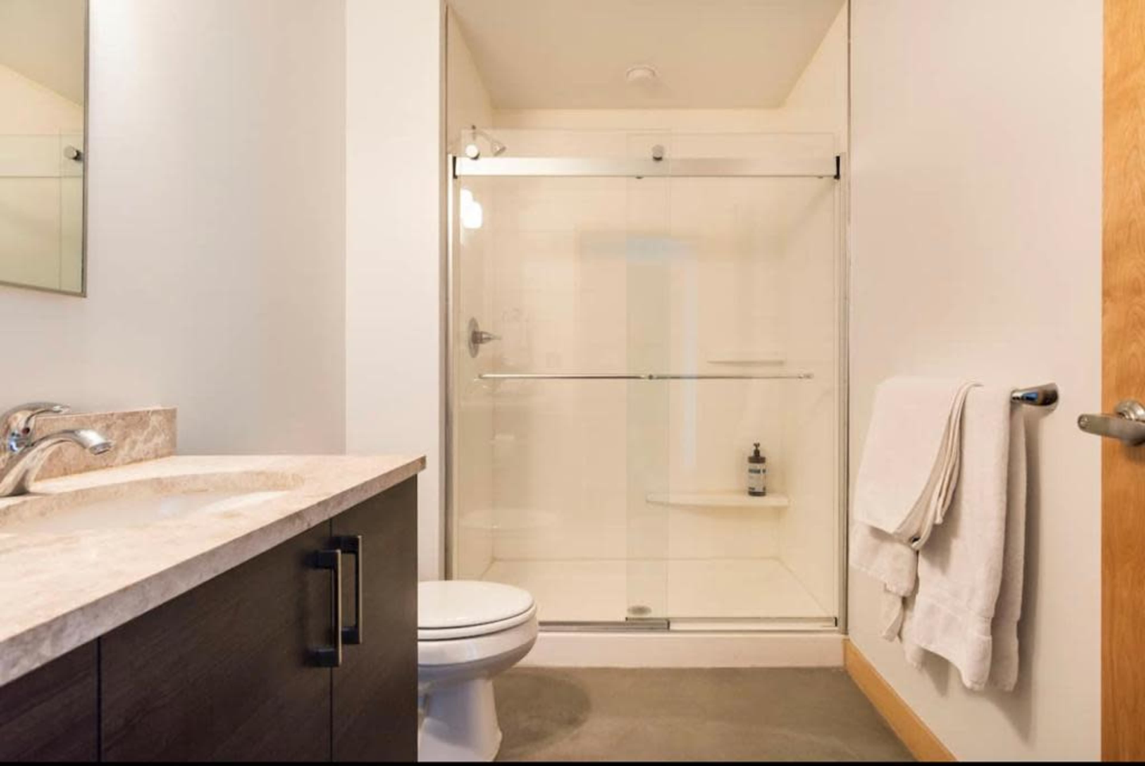 A modern bathroom featuring a glass shower enclosure, a countertop sink, a toilet, and a towel hanging on a holder.