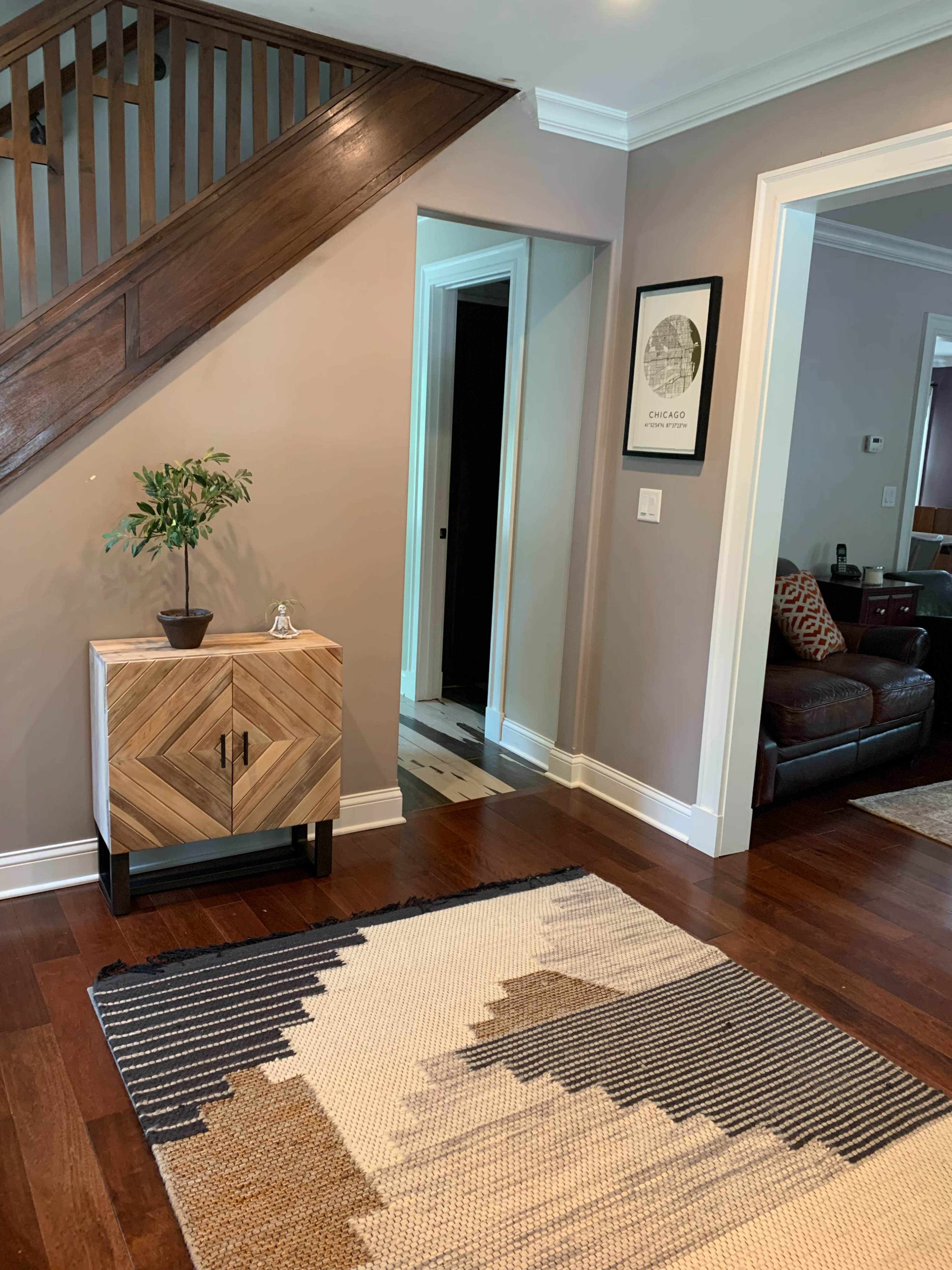 A foyer with a patterned rug, a wooden cabinet with a geometric design, and a staircase leading to an upper level.
