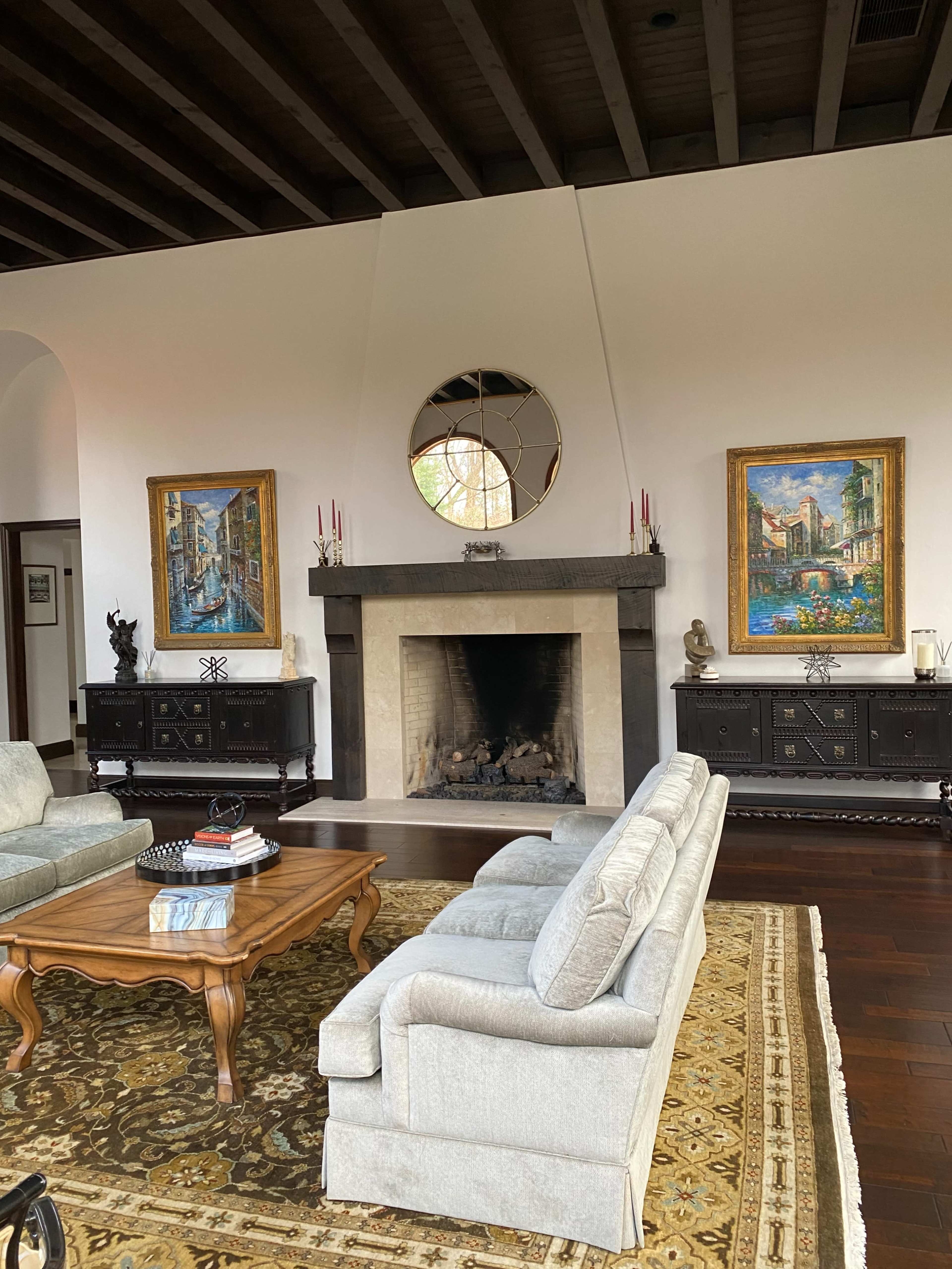 The room features a cozy living area with a fireplace, two paintings on the walls, and a coffee table in front of a light gray sofa.