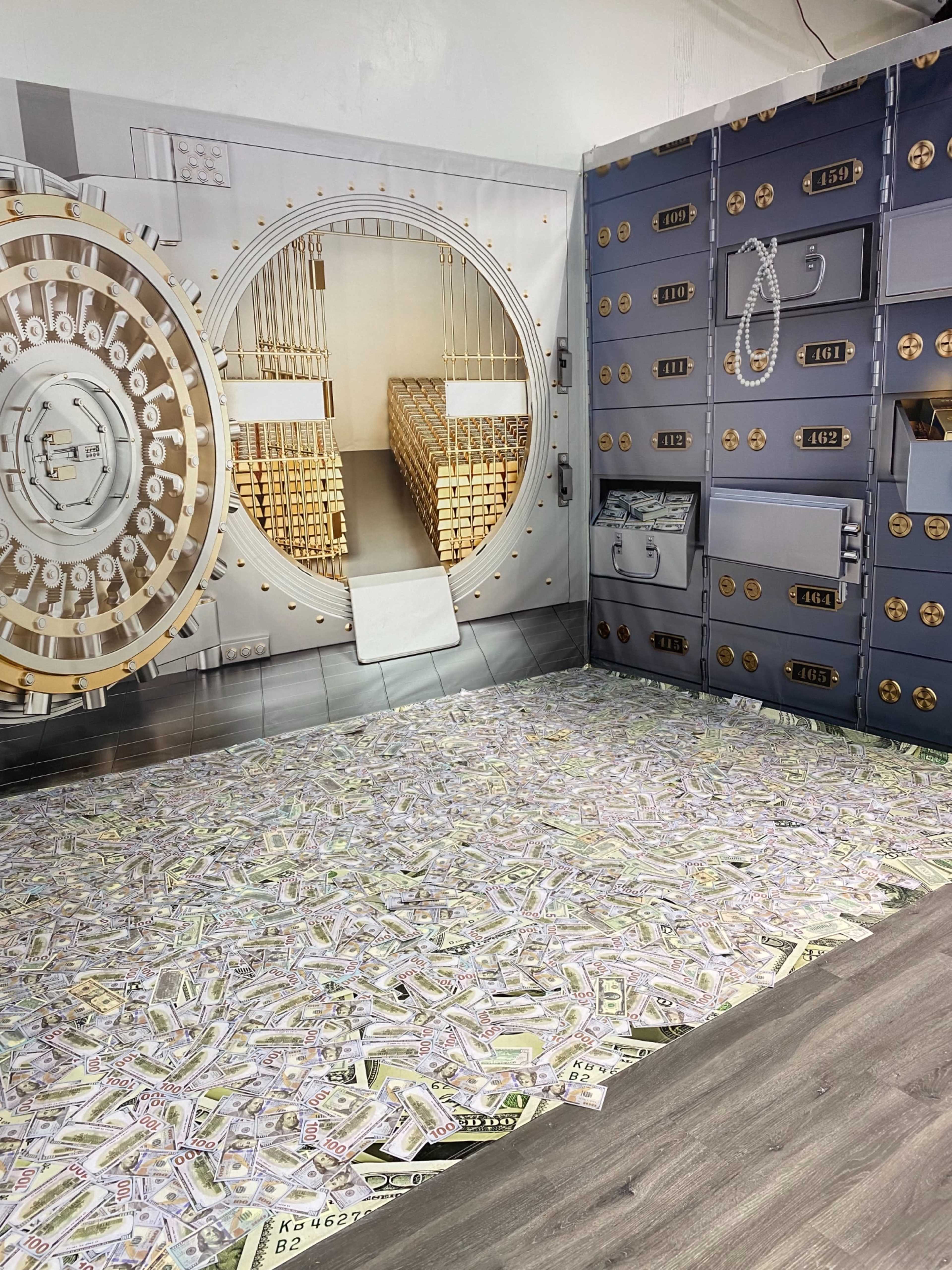 A room designed to look like a bank vault, with a large vault door, gold bars in the background, and a floor covered in imitation stacks of cash.