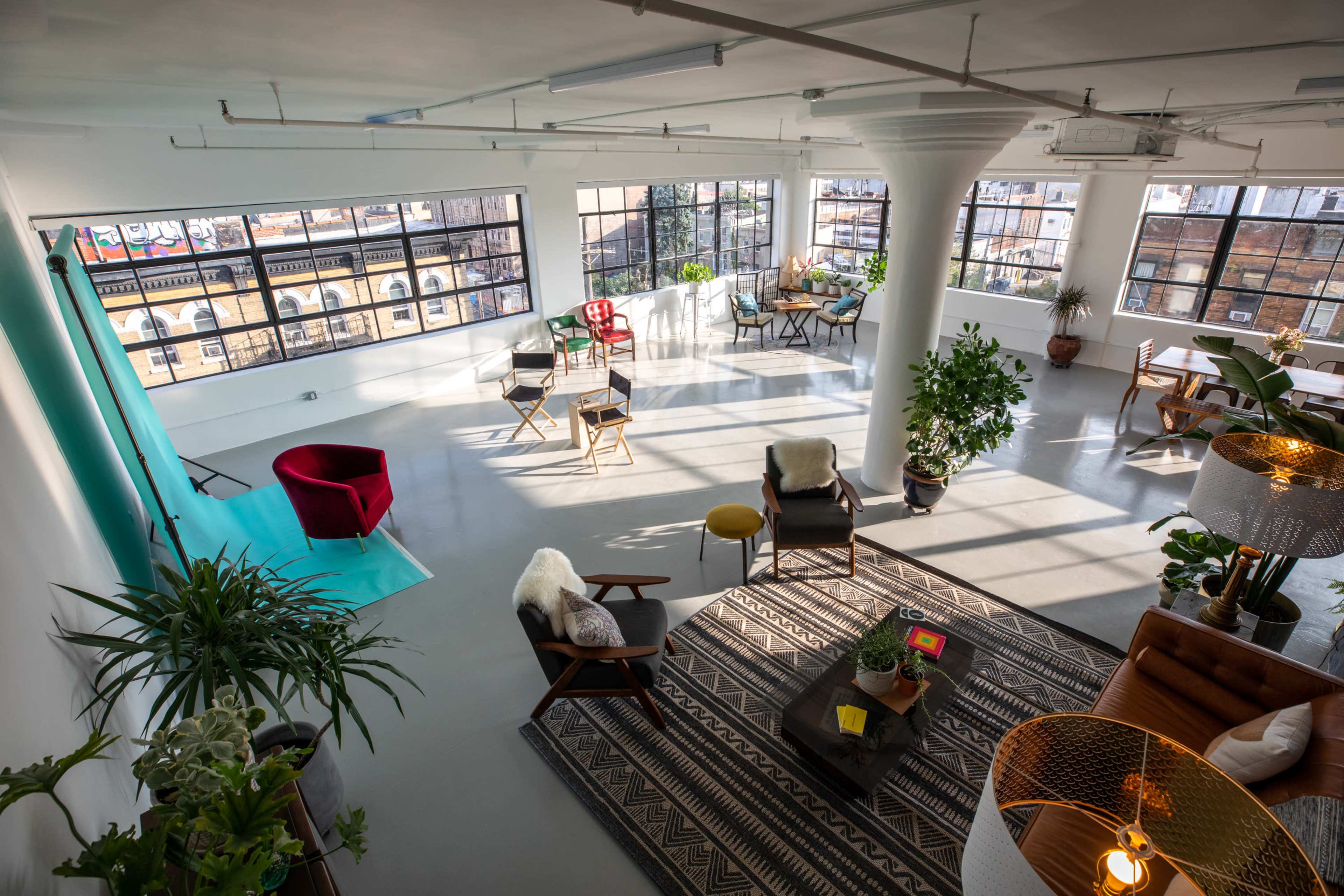 A bright, spacious studio with large windows, various seating arrangements, and indoor plants.