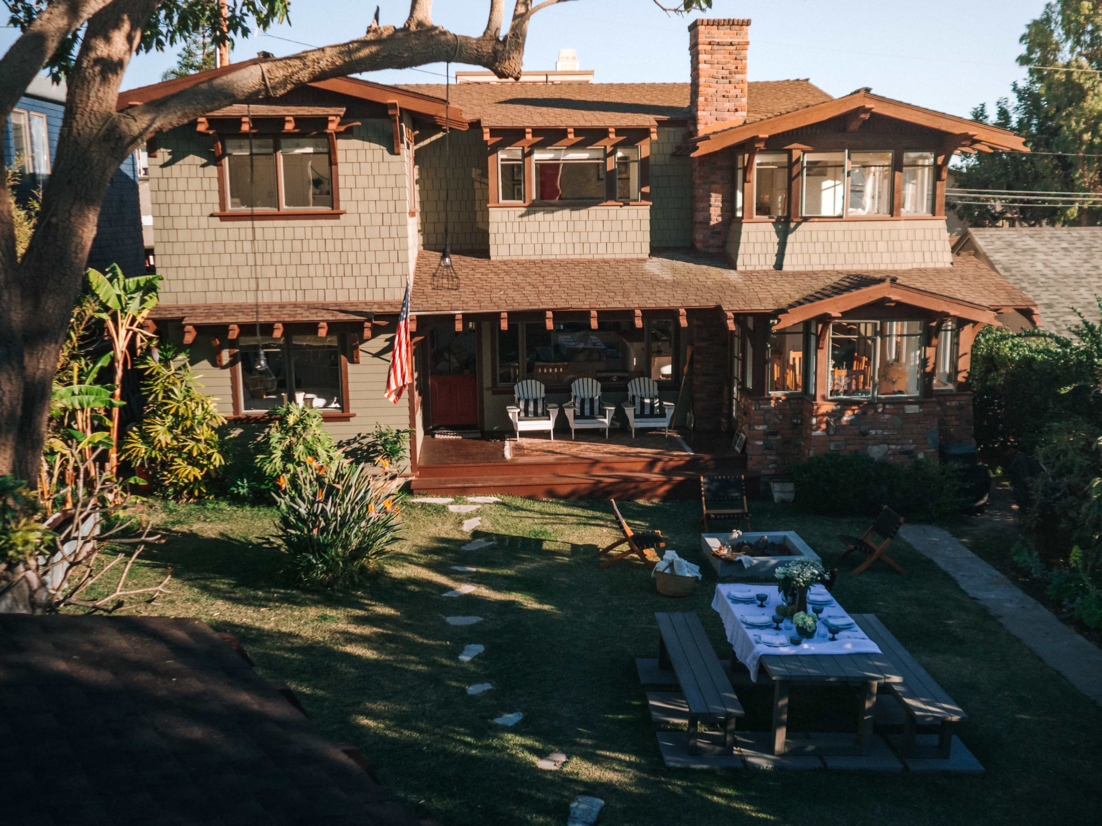 A two-story, craftsman-style house with a front porch and a well-maintained lawn, featuring outdoor seating and an American flag.