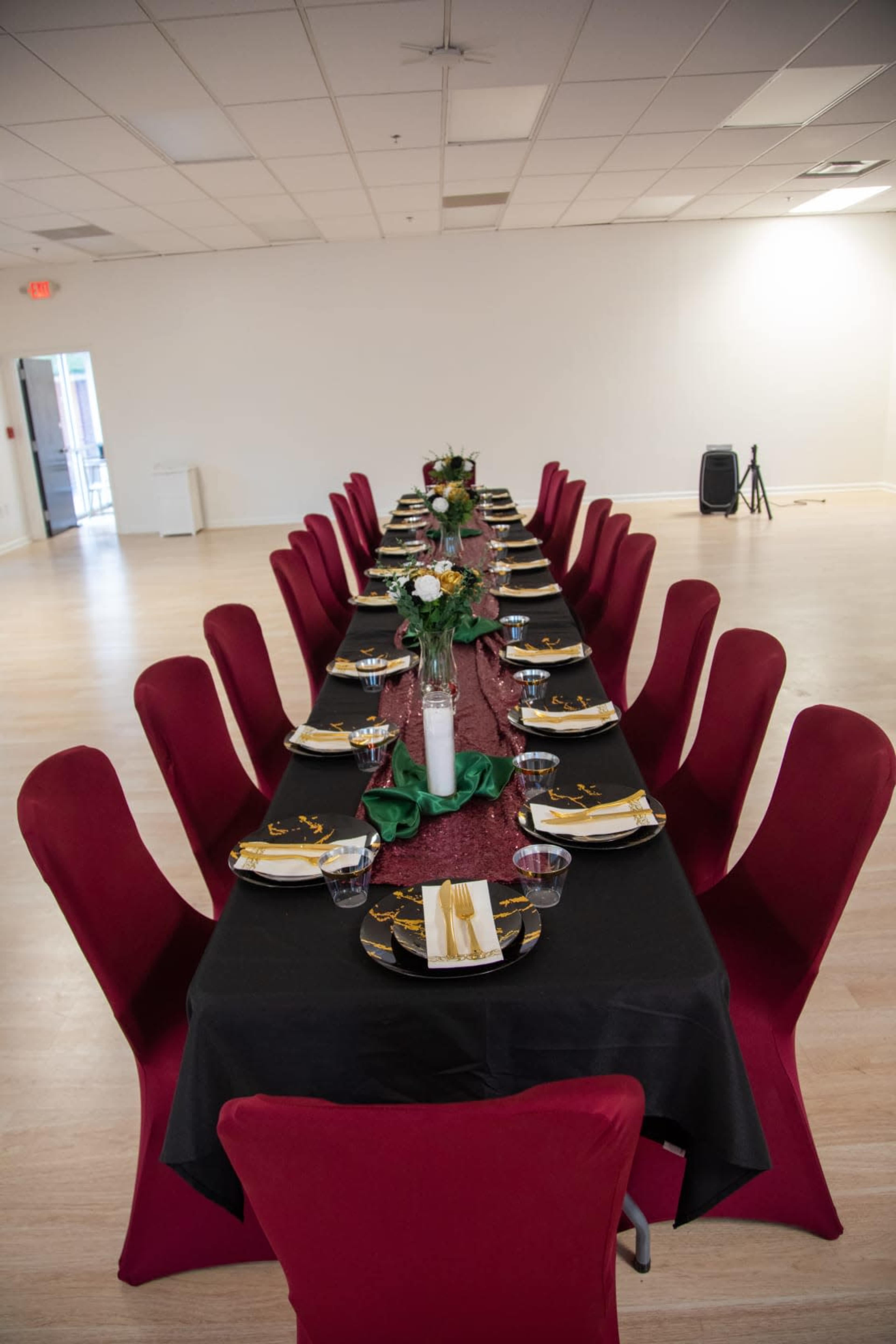 A long dining table is set with black tablecloths, red chairs, and decorative centerpieces, ready for an event.