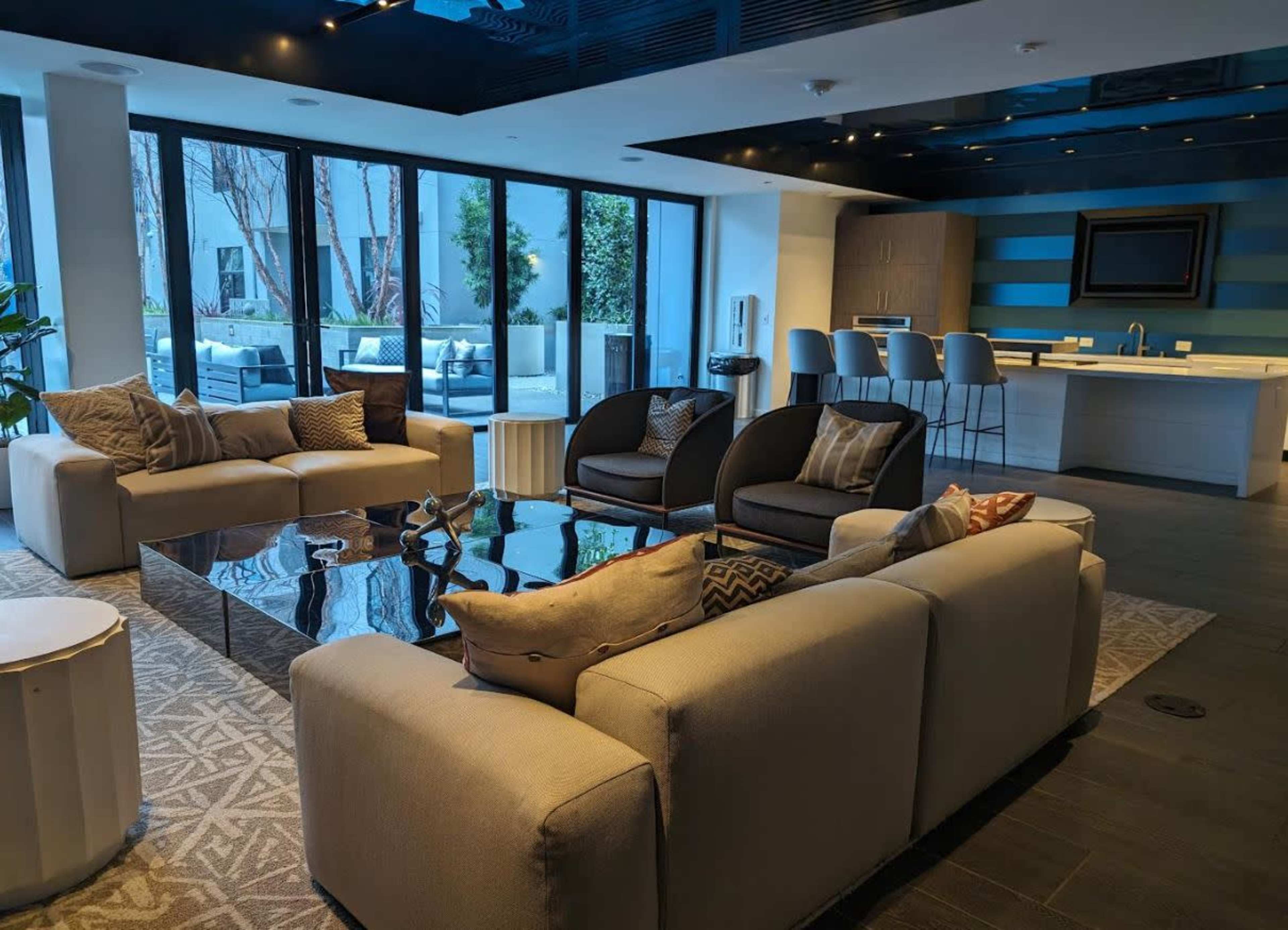 A modern living space with a seating area featuring sofas and chairs, a coffee table, and a view of an outdoor area through large windows.