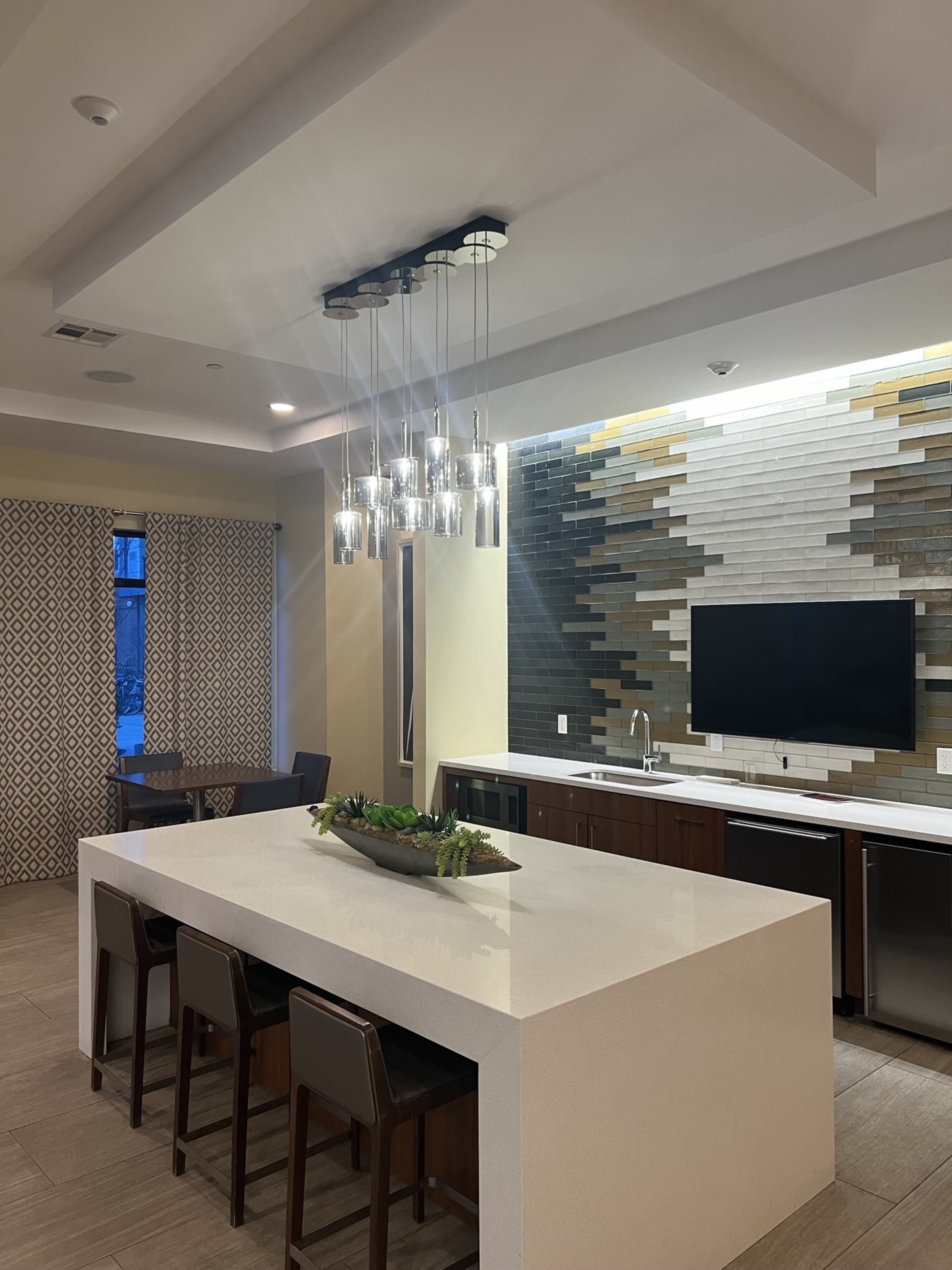 A modern kitchen with a large white island, pendant lights above, and a wall featuring a textured tile design.