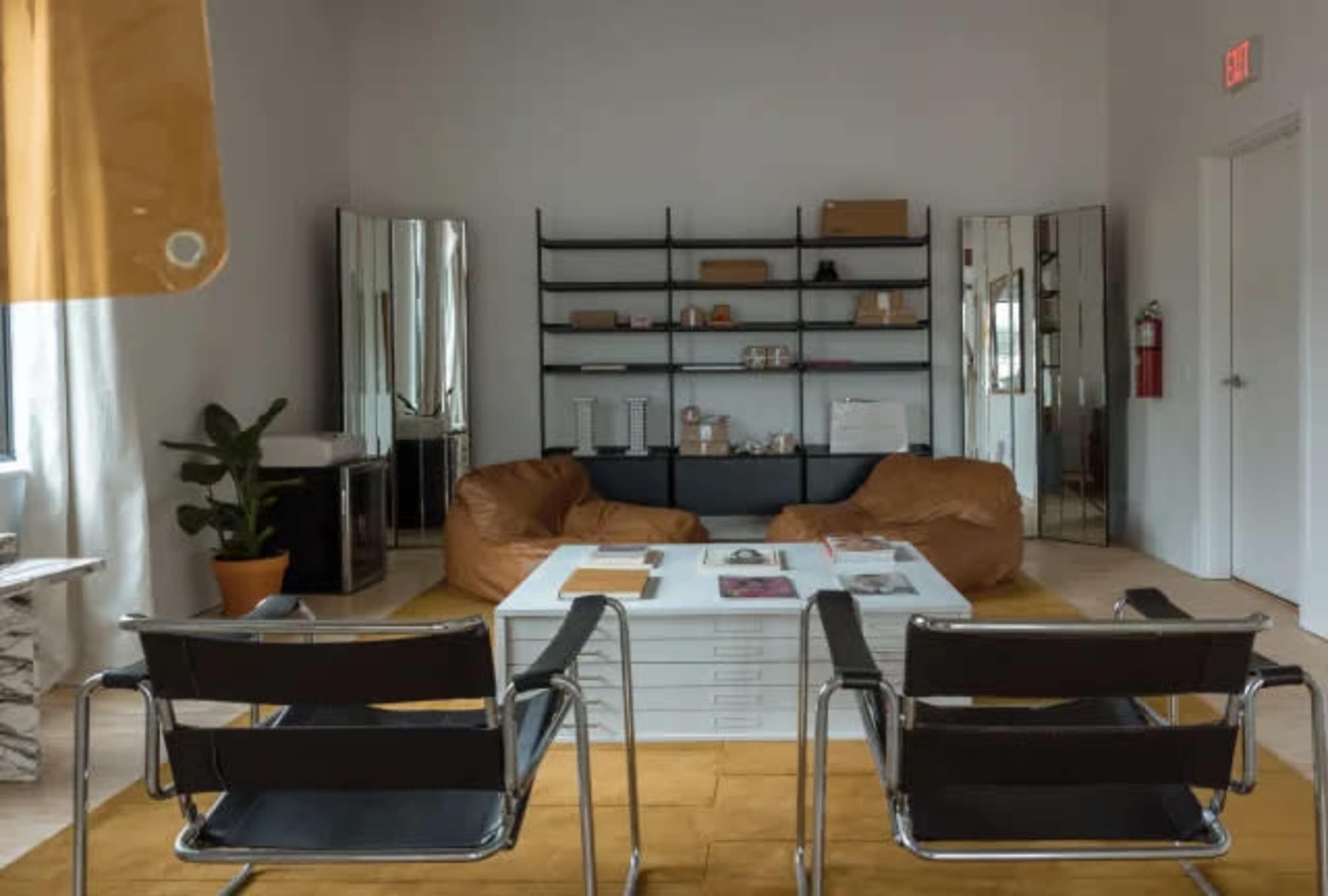 The image shows a modern sitting area featuring two bean bag chairs, a white coffee table, a black shelving unit, and large mirrors against the wall.
