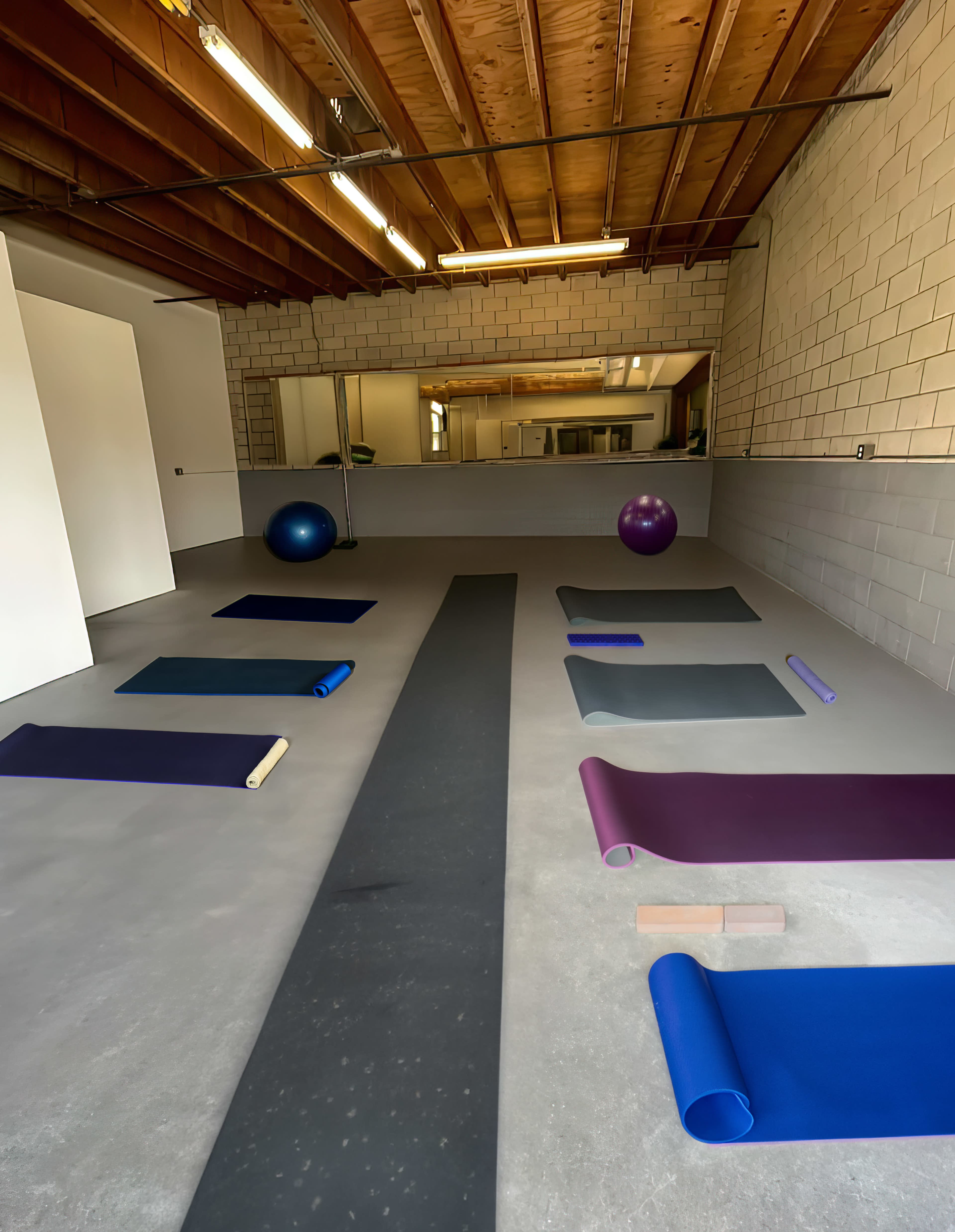 A spacious and minimally furnished exercise room with several yoga mats and exercise balls arranged on the floor.