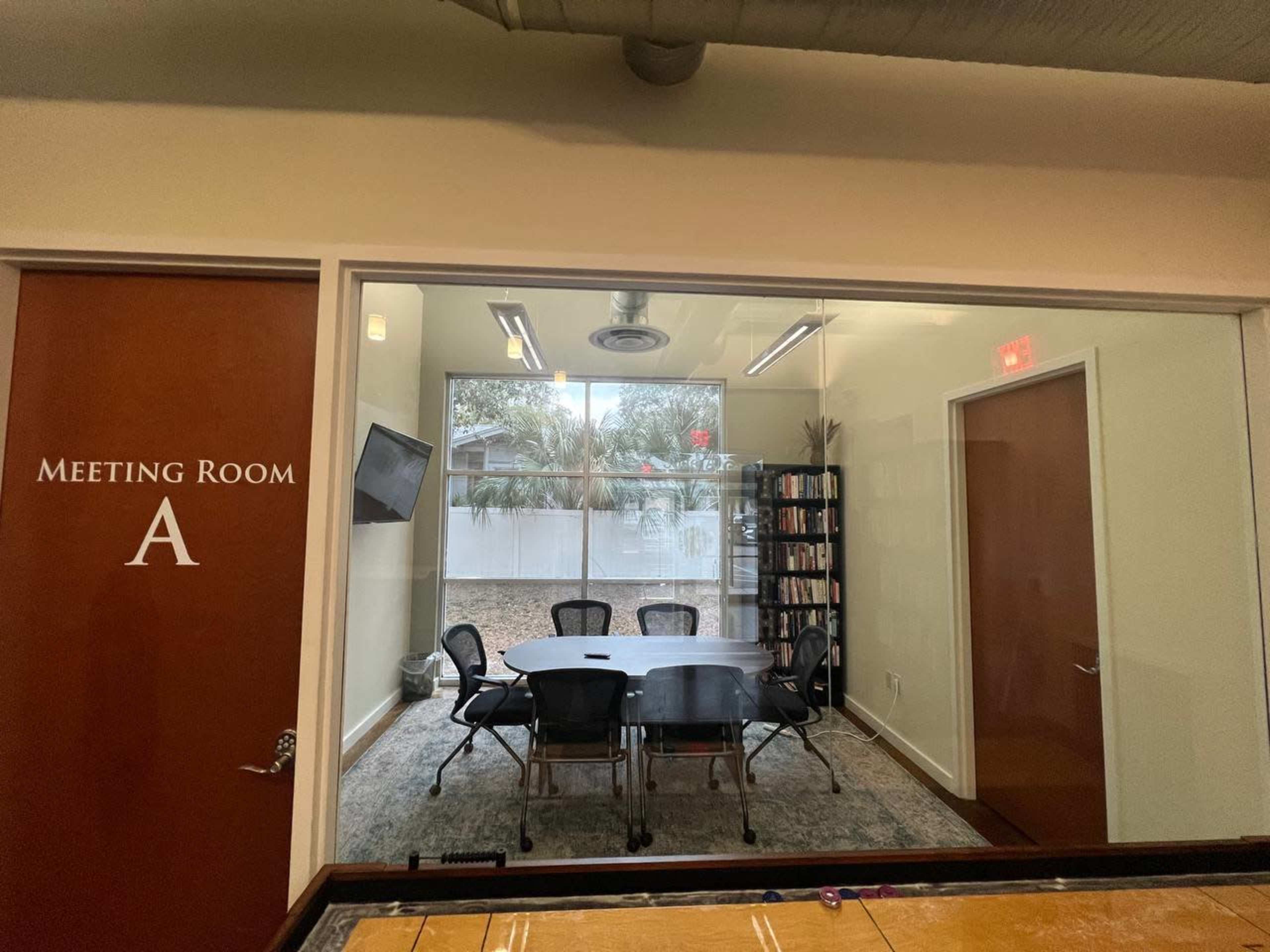 A meeting room labeled "Meeting Room A," featuring a table surrounded by chairs and a window with a view of an outdoor area.