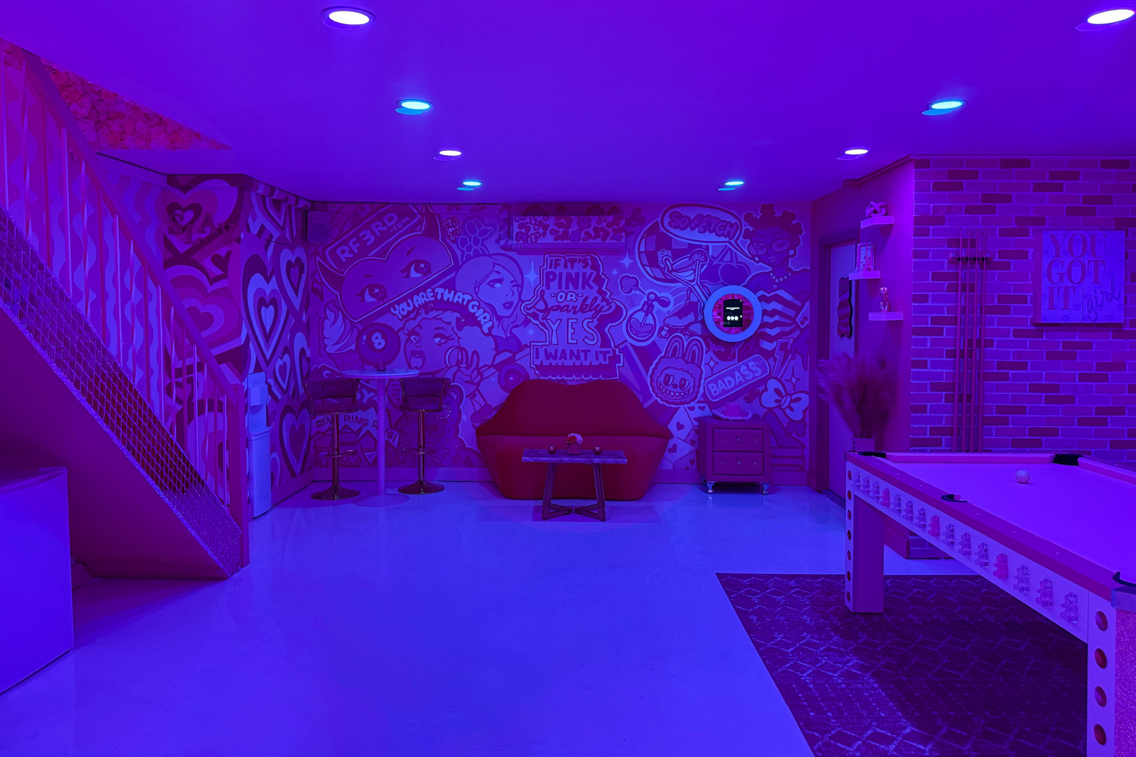 The room features vibrant purple lighting with colorful graffiti on the walls, a red couch, and a pool table.