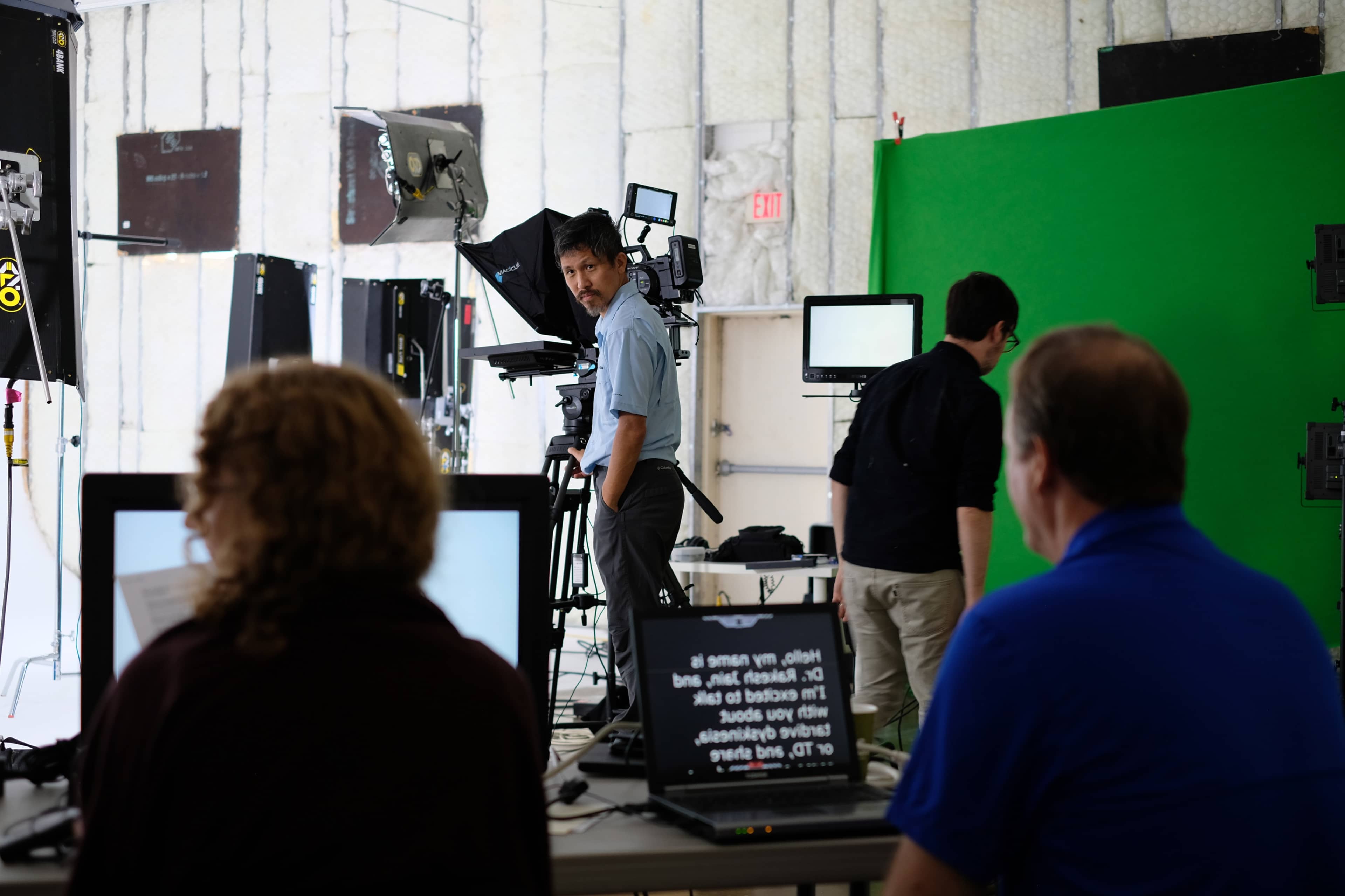 A studio setup features cameras and monitors, with crew members operating equipment and preparing for a shoot.