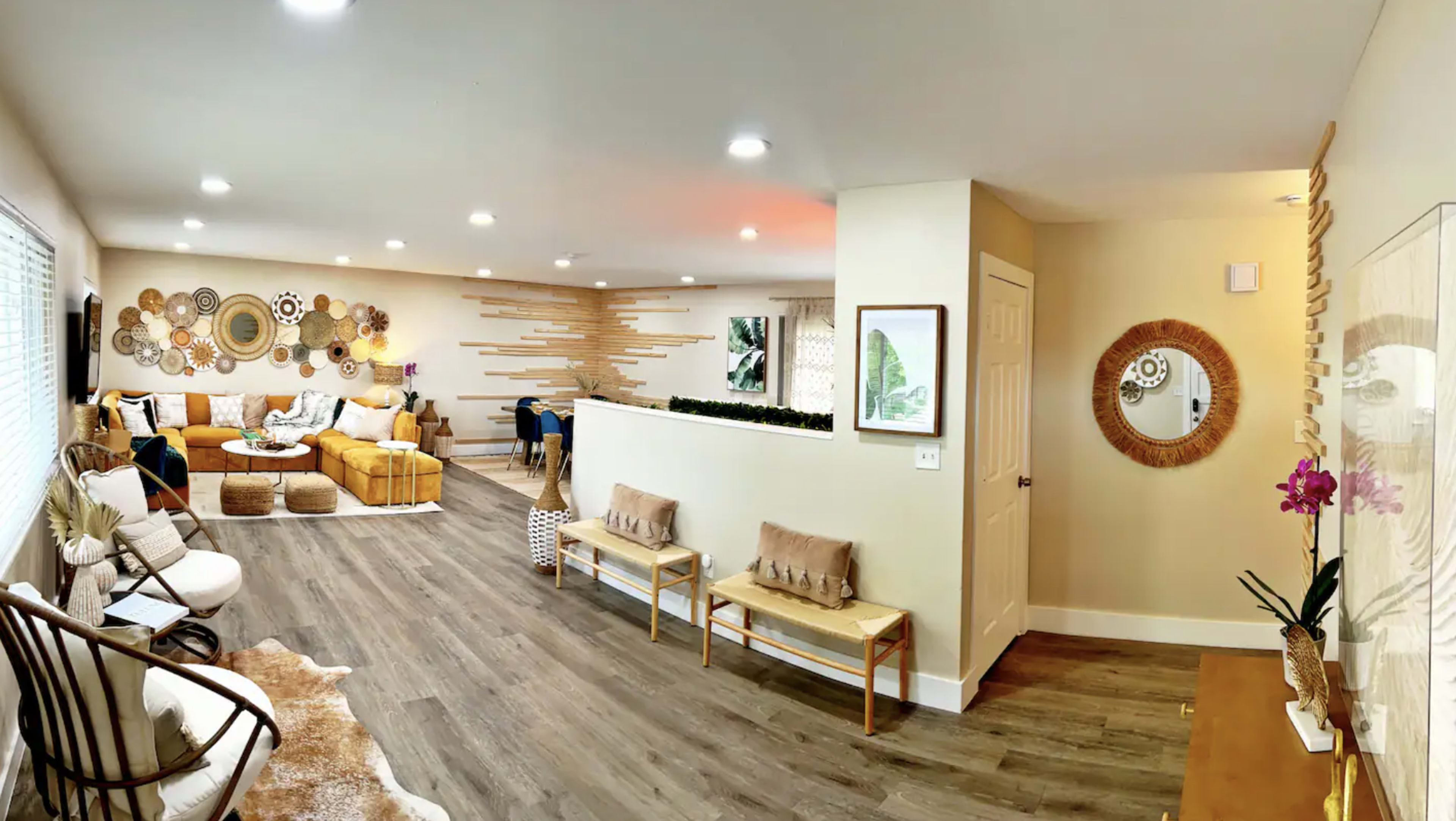 The image shows a spacious living area featuring a sectional sofa, decorative wall art, and a hallway leading to another room with seating arrangements and a mirror.