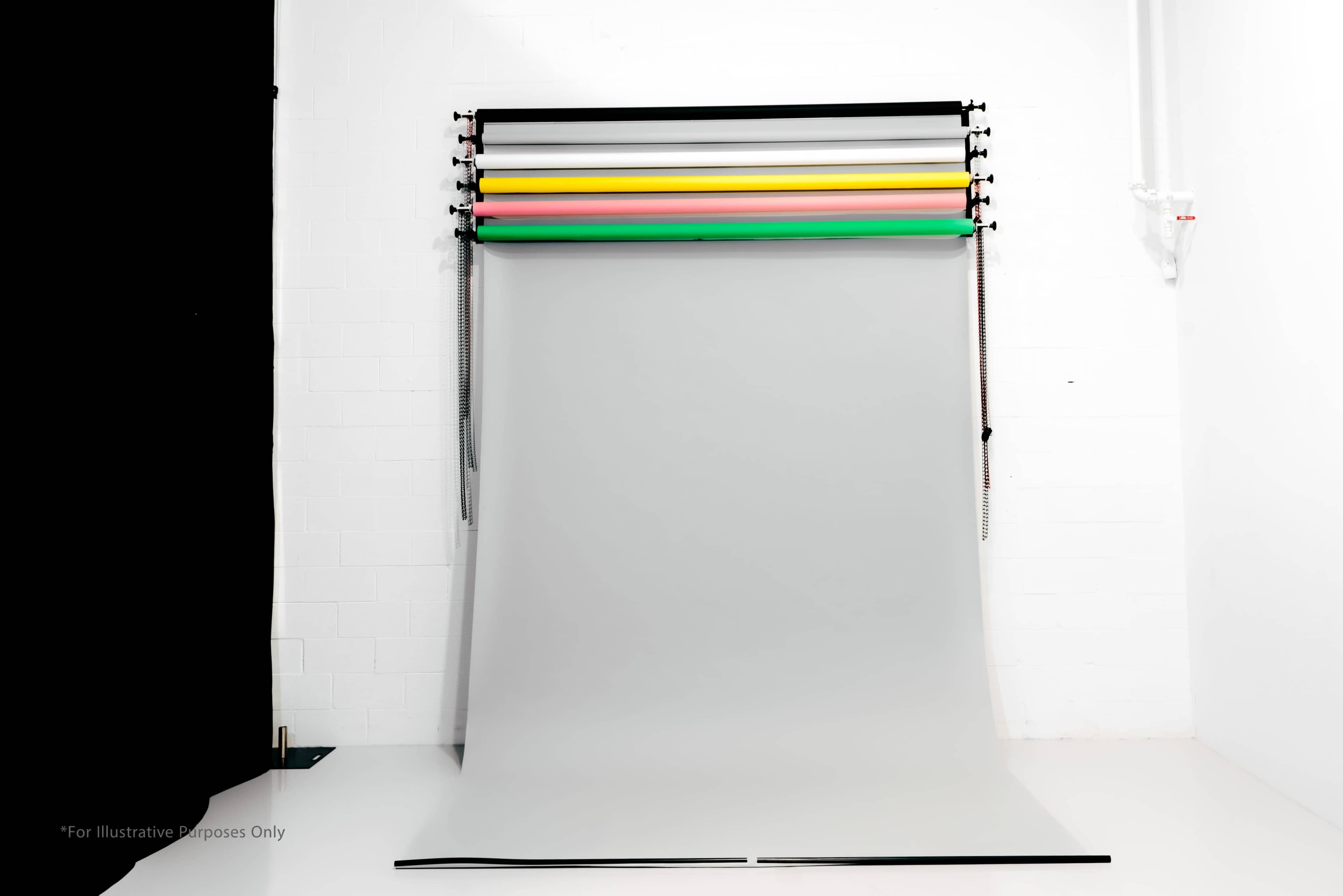 A backdrop setup featuring several colored rolls mounted above a plain grey backdrop against a white wall.