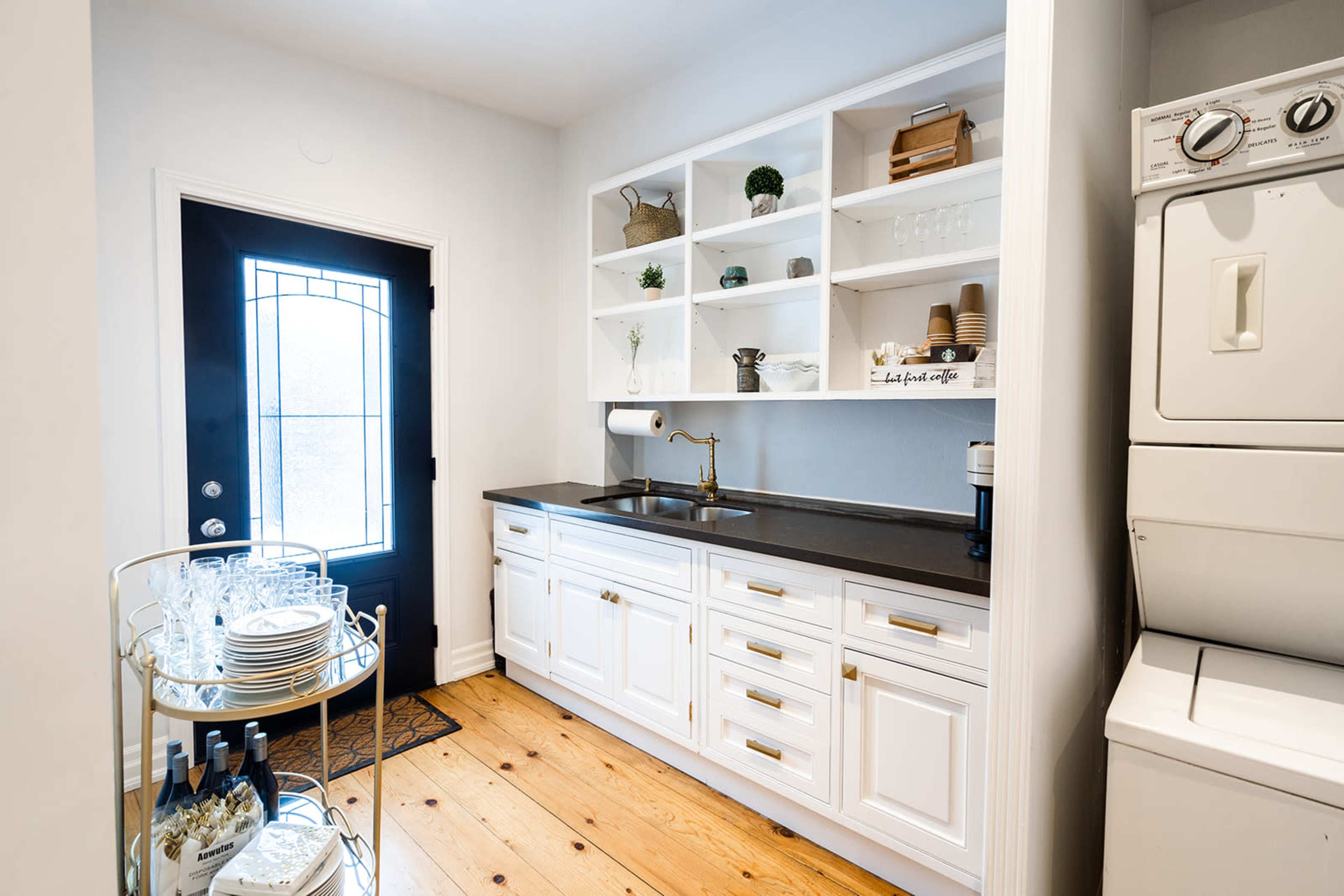 A compact kitchen area with white cabinetry, a black countertop, a sink, and a laundry unit beside a black door, all set against a light-colored wall.