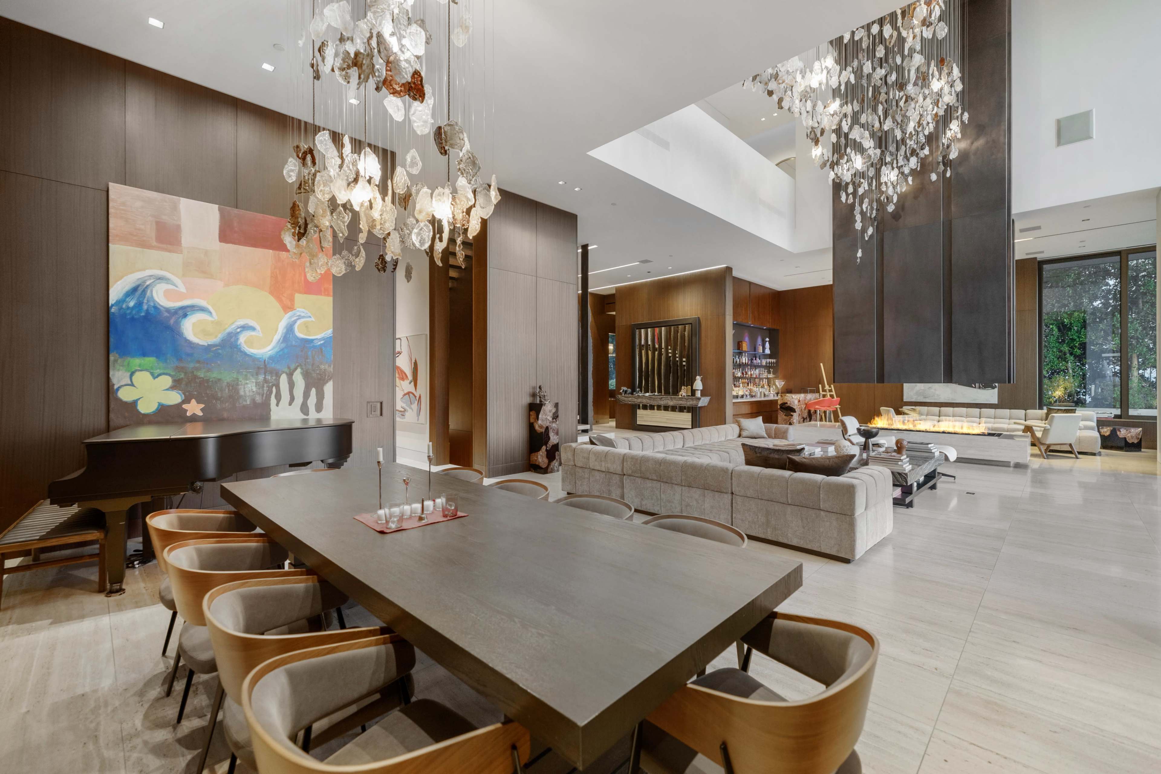 The image shows a modern living and dining area featuring a grand piano, a large dining table with wooden chairs, and a contemporary fireplace.