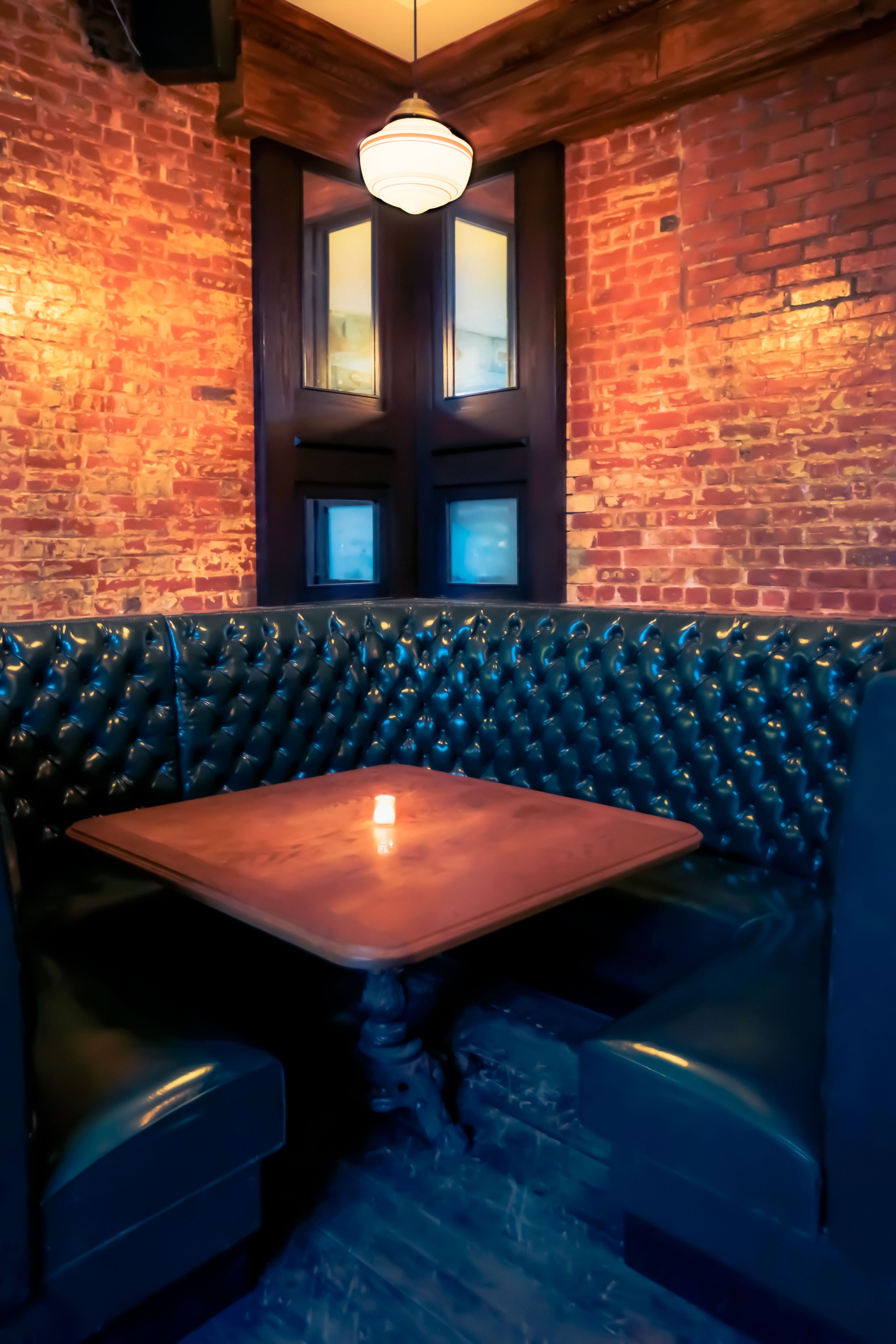 A cozy booth with tufted black leather seats and a wooden table, set against a backdrop of exposed brick walls.