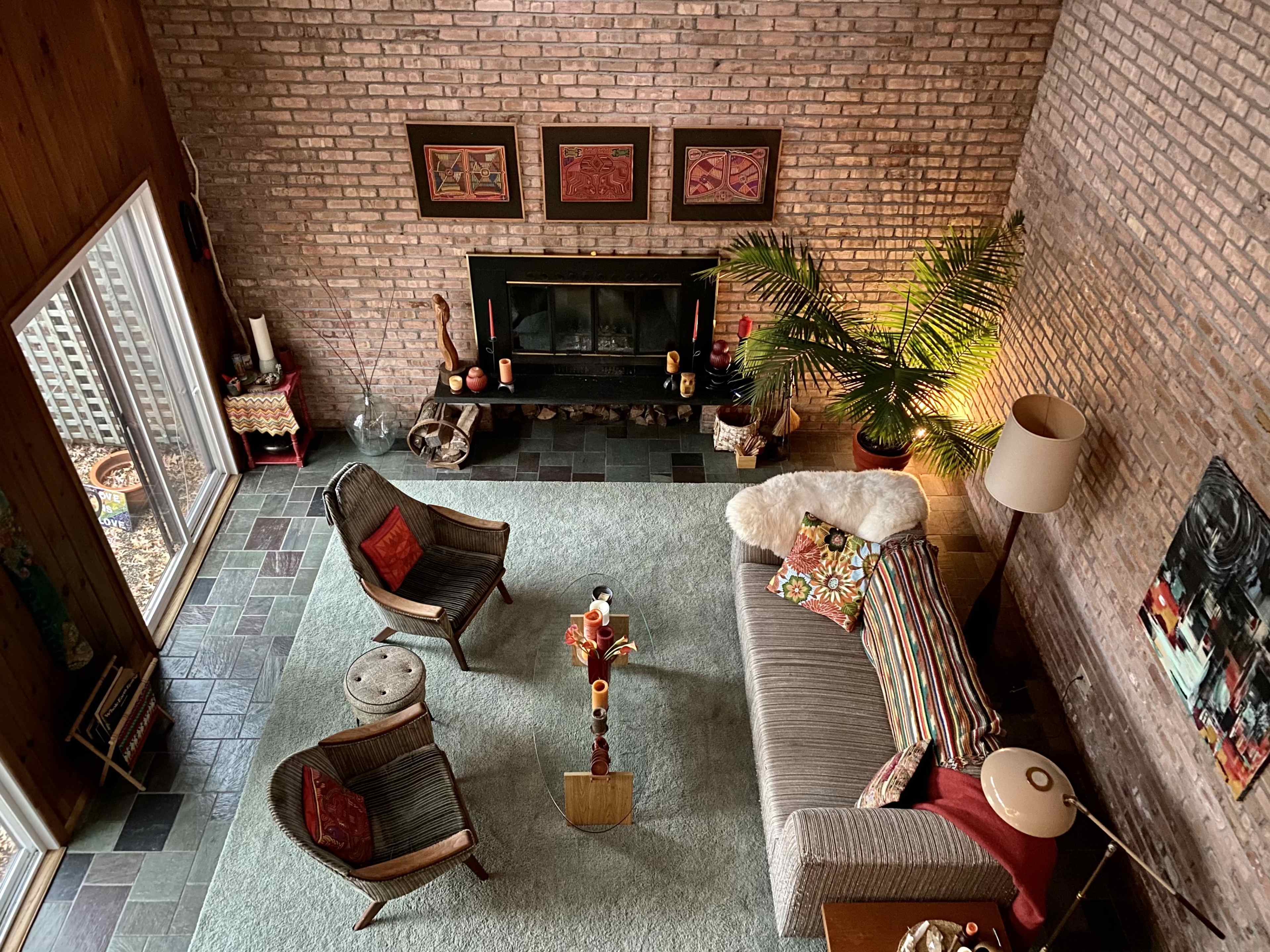 The image shows a cozy living room with a brick wall, a fireplace, a sofa adorned with patterned cushions, and two wooden chairs, all arranged around a coffee table.