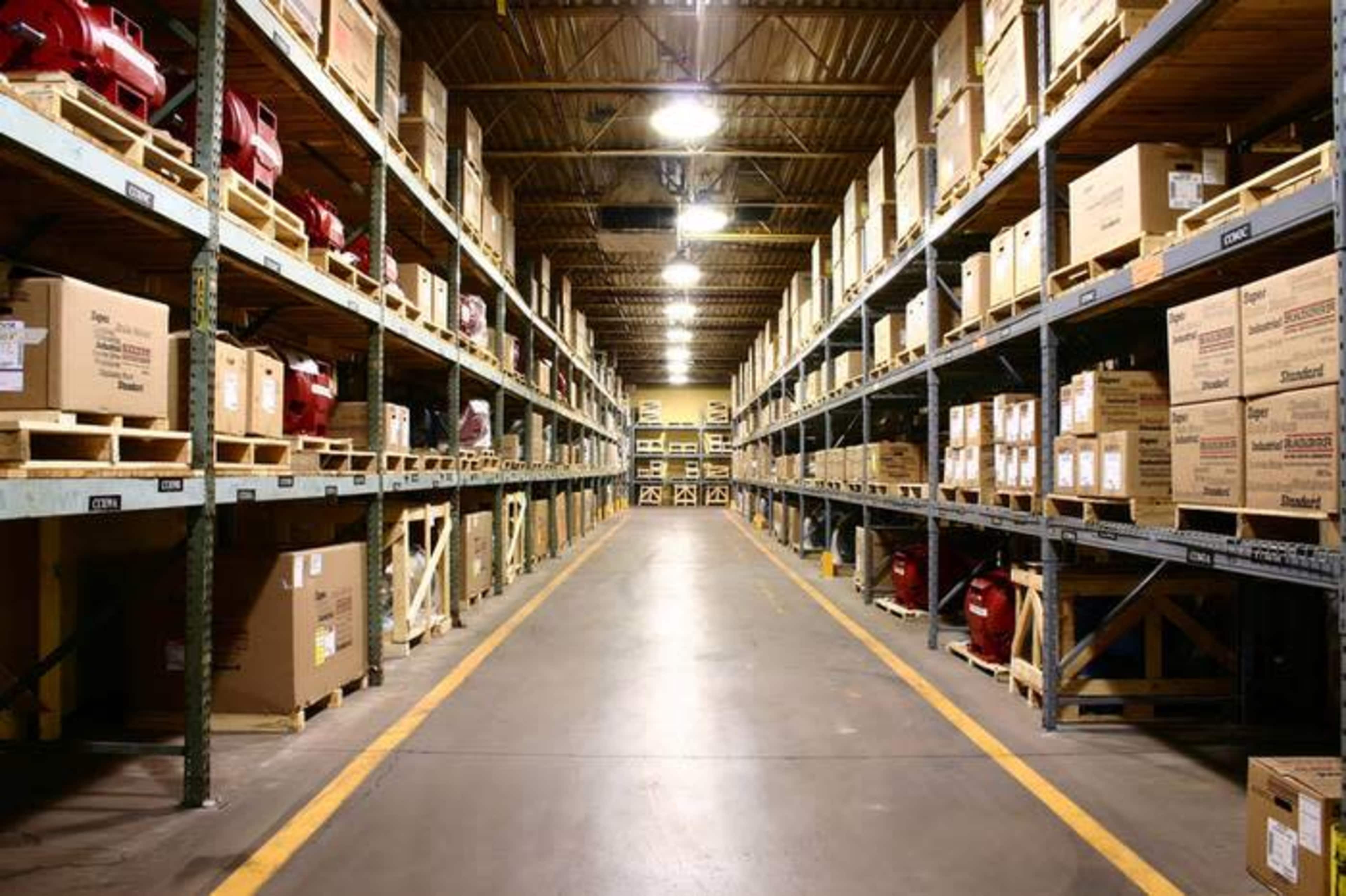 An organized warehouse aisle with shelves stacked high with boxes and equipment on either side.