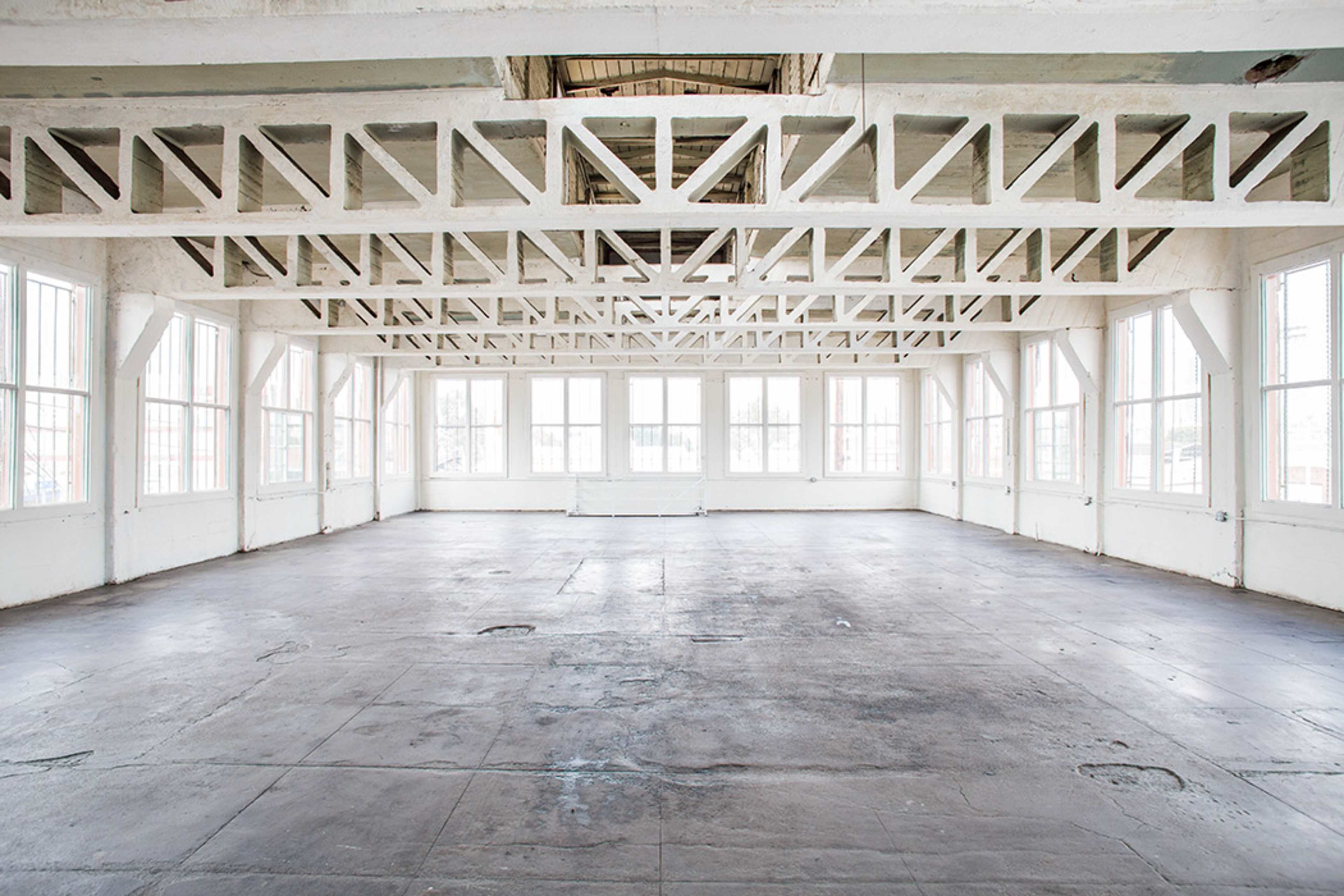 A spacious, empty room with large windows and exposed wooden beams along the ceiling.